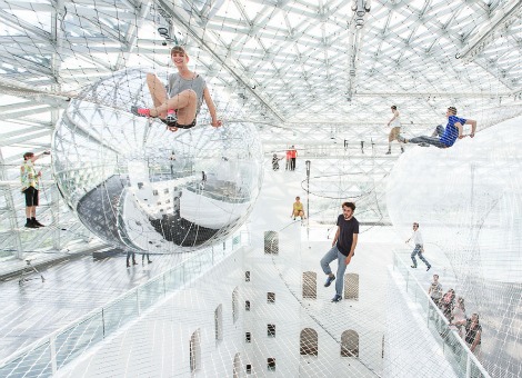 Wandelen door de lucht was nog nooit zo dichtbij. Kunstenaar Tomás Saraceno bouwde een 'speeltuin' van netten op 25 meter hoogte. Het kunstwerk genaamd In Orbit beslaat 2500 vierkante meter boven in een gebouw in de Duitse stad Düsseldorf. De netten zijn gemaakt van staal en wegen in totaal zo'n 3000 kilo. Boven op de netten liggen ballen van 300 kilo. Bij elke stap die de bezoeker zet, reageert de complete installatie. Bekijk hieronder een video van het kunstwerk. Voor meer foto's van de installatie, zie de website van Tomás Saraceno.