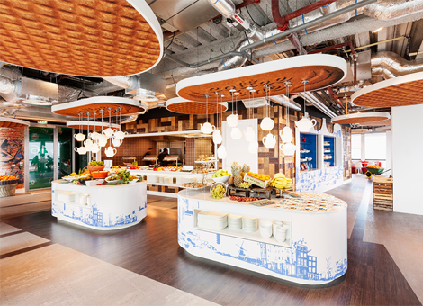 De inrichting van het nieuwe kantoor van Google in Amsterdam is geïnspireerd op de garage waar Larry Page en Sergey Brin het zoekbedrijf ooit oprichtten. Het kantoor van Google Nederland aan de Amsterdamse Zuidas heeft een opfrisbeurt gekregen. Vorige week leverde ontwerpbureau D/Dock het gebouw op. De 'garage' is voorzien van Nederlandse elementen. De balie bij de receptie heeft de vorm van een bakfiets en de plafondplaten lijken op stroopwafels. Op zoek naar een oplader voor je computer? Kijk maar even in de Febo-automatiek; daar kun je computer accessoires uit de muur trekken in plaats van kroketten. Een oude caravan op de 15e verdieping doet dienst als informele meeting room. Meditatiekamer en deskbikes Coen van Dijck, partner van D/DOCK, noemt het nieuwe Google kantoor een 'feelgood-kantoor'. "Het is een plek die mensen beter laat functioneren door een werkomgeving te creëren die aan ieders behoeften voldoet", aldus Van Dijck. "Geluk, comfort, flexibiliteit, ontspanning, beweging, daglicht, frisse lucht, visuele stimulans en een uitgebalanceerde catering zijn fundamentele elementen die dit kantoor een gezond kantoor maken." Om de werknemers fit te houden, biedt Google een gezond ontbijt en lunch aan in het restaurant. Daarnaast is er een meditatiekamer en kunnen de echte gezondheidsfreaks gebruikmaken van deskbikes, een combinatie van een hometrainer en een bureau. Het kantoor is via Google Street View te bezoeken. Hieronder nog wat meer plaatjes.