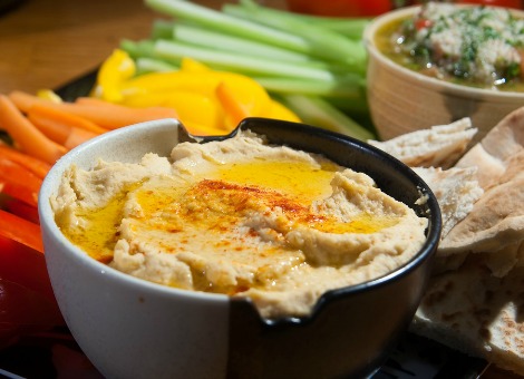 Hummus is in steeds meer supermarkten, koelkasten en restaurants te vinden. Lekker voor op brood of om mee te dippen. Maar is dat wel zo gezond? En mag je hummus zonder kikkererwten nog steeds hummus noemen? In bijna alle supermarkten is het tegenwoordig te vinden: hummus, de puree van kikkererwten die oorspronkelijk uit het Midden-Oosten komt. De spread is met name populair in de grote steden, en wordt bijvoorbeeld op hippe broodjes gesmeerd als vervanger van mayonaise. Of als bijgerecht geserveerd bij falafel. In de simpelste vorm bestaat hummus uit gepureerde kikkererwten, tahin (sesamzaadpasta), olijfolie, knoflook en enkele kruiden. Dat is alles. "Het is vegetarisch, heeft veel smaak en peulvruchten zijn duurzaam om te verbouwen", zegt culinair journalist Onno Kleyn. "Het past dus in veel hokjes", zo verklaart hij de populariteit van hummus. "Bovendien is walgelijk gezond", aldus Kleyn, die deel uitmaakt van De Bruine Bonenbende, een weblog over peulvruchten. "Kikkererwten zijn net als andere peulvruchten bijzonder voedzaam. Ze bevatten de traagste koolhydraten die er bestaan." Hoe gezond is hummus? Maar is de kikkererwtenspread die je in de supermarkt koopt wel echt zo gezond? Kant-en-klare varianten bevatten bijna twee keer zoveel kilocalorieën als zelfgemaakte hummus, blijkt uit een inventarisatie van Z24. [google-drive number='1'] Met name het aantal grammen vet ligt aanzienlijk hoger bij bekende merken als Sabra en Maza, en de huismerken van verschillende winkels. Dat wijst erop dat fabrikanten extra plantaardige olie toevoegen, wellicht om de hummus smeuïger te maken. Plantaardige, onverzadigde vetten Toch raadt diëtiste Katinka Huiskamp het eten van hummus niet af. "Qua calorieën zou je een kant-en-klare hummus kunnen vergelijken met smeerleverworst", laat ze via e-mail weten. "Beide bevatten circa 300 kcal per 100 gram. Het verschil: de vetten uit hummus zijn van het gezonde plantaardige onverzadigde soort, terwijl smeerleverworst minder gezonde dierlijke verzadigde vetten bevat", aldus Huiskamp. "Je krijgt met de kant-en-klare hummussen veel waar voor je geld." Tot die conclusie komt Kleyn ook. Hummus maakt min of meer dezelfde opmars als pesto een aantal jaar geleden. Maar in tegenstelling tot pesto liggen bij hummus de versie uit de fabriek en de zelfgemaakte variant qua smaak "redelijk dichtbij elkaar". Dat komt volgens Kleyn omdat de receptuur van hummus een conserveringsmiddel bevat: "Meestal doe je er wat citroen bij om het op smaak te brengen." Bij pesto voegen fabrikanten noodgedwongen zuren toe die er eigenlijk niet in horen om de houdbaarheid te verlengen. Dat gaat ten koste van de smaak. Smaaktest: Sabra en Maza het lekkerst Waar moet een goede hummus aan voldoen? "Smaken verschillen natuurlijk", zegt Kleyn. "In het Midden-Oosten zijn er net zoveel hummussmaken als bereiders. Maar ik vind het lekker als het bittere van de tahin proefbaar aanwezig is. En zonder knoflook werkt het ook niet." Z24 besloot de proef op de som te nemen en kocht tien verschillende merken hummus. Daaruit kwamen Sabra en Maza als duidelijke winnaars naar voren. Het testpanel van tv-programma Kassa kwam eerder tot dezelfde conclusie. Beide hummussen zijn licht van kleur, goed smeerbaar en fijn van structuur. [google-drive number='3'] Biologische merken als Florentin, Hobbit en Benny Moshel vallen niet in de smaak. Deze zijn over het algemeen iets droger, grover van structuur en vlakker van smaak. Buitenbeetje is de hummus van de Aldi, waar zongedroogde tomaat aan toe is gevoegd. Die smaak overheerst dusdanig dat de kikkererwten en sesamzaadpasta nauwelijks te proeven zijn. Hummus zonder kikkererwten Opvallend is dat het percentage kikkererwten sterk uiteenloopt bij de verschillende merken, van 32 tot 64 procent. Ook tussen de als best geteste producten van Sabra en Maza zit een groot verschil. [google-drive number='2'] Hoewel kikkererwten het hoofdingrediënt zijn van hummus, lijkt het percentage niet bepalend voor de smaak. Sterker nog: er is zelfs hummus op de markt die helemaal geen kikkererwten bevat. In de VS maakt fabrikant Tryst Gourmet hummus die gemaakt is van gepureerde linzen, witte bonen, zwarte bonen en sinds kort zelfs wortels en bieten. Daarmee liften ze mee op de groeiende populariteit van de kikkererwtenspread. Dit tot groot ongenoegen van concurrent Sabra, die middels een petitie de Amerikaanse voedsel- en warenautoriteit oproept om het product te reguleren. Hummus zonder kikkererwten zou geen hummus mogen heten. In Nederland gaat Maza bij hun stand in de Amsterdamse Foodhallen experimenteren met hummus van doperwten, vertelt commercieel directeur Roberto Oberegger. "Maar we kunnen het ook een andere naam geven. Daar zijn we nog niet over uit." De Nederlandse Voedsel- en Warenautoriteit (NWVA) laat weten dat het onwaarschijnlijk is dat er op korte termijn regelgeving komt voor hummus. Dat zou op Europees niveau moeten worden geregeld, op dezelfde manier als bijvoorbeeld parmaham en Edammer kaas beschermde streekproducten zijn. Maar hummus is geen Europees product. "Producenten kunnen doen wat ze willen", zegt woordvoerder Lex Benden van de NWVA. "Wij zeggen altijd: kijk op de labels. Dan weet je wat erin zit." Het verschijnsel hummus Culinair journalist Kleyn is niet verrast dat hummus de oorspronkelijke betekenis voorbij lijkt te streven. "In principe kun je alle peulvruchten pureren. Technisch gezien mag je dat dan geen hummus noemen, maar het gaat meer om het verschijnsel. Hummus staat voor een mediterraanse spread waar je dingen in kunt dippen." De naam gaat volgens Kleyn een eigen leven leiden, zoals ook is gebeurd met tapenade. "Tapéno is het Provençaalse woord voor kappertje", zegt Kleyn. "Inmiddels is tapenade een synoniem geworden voor olijvenprut." Lees ook De nieuwe superfood heet maca, maar de Chinezen kopen alles op Dit zijn de 10 duurste wijnen ter wereld De foodtruck: in crisistijd dé uitkomst voor restaurateurs