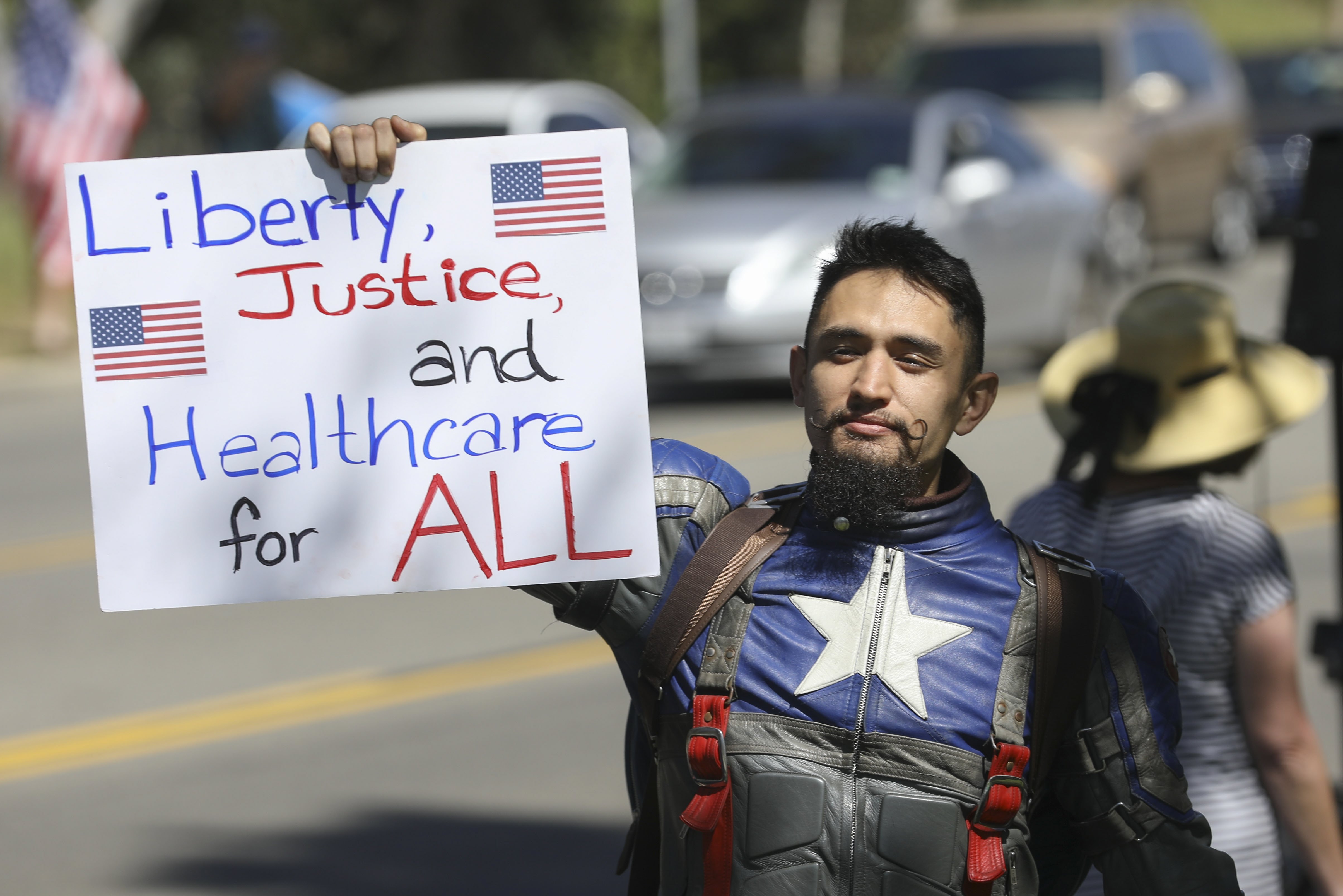 2017-04-04 09:40:21 epa05888357 Chris Hayward, dressed as Captain America, joins hundreds of Anti-Trump protesters demonstrate against the possible repeal of Obamacare, the Russian investigation and the Gorsuch Supreme Court vote outside the office of Republician Rep. Darrell Issa in Vista, California, USA, 04 April 2017. EPA/EUGENE GARCIA