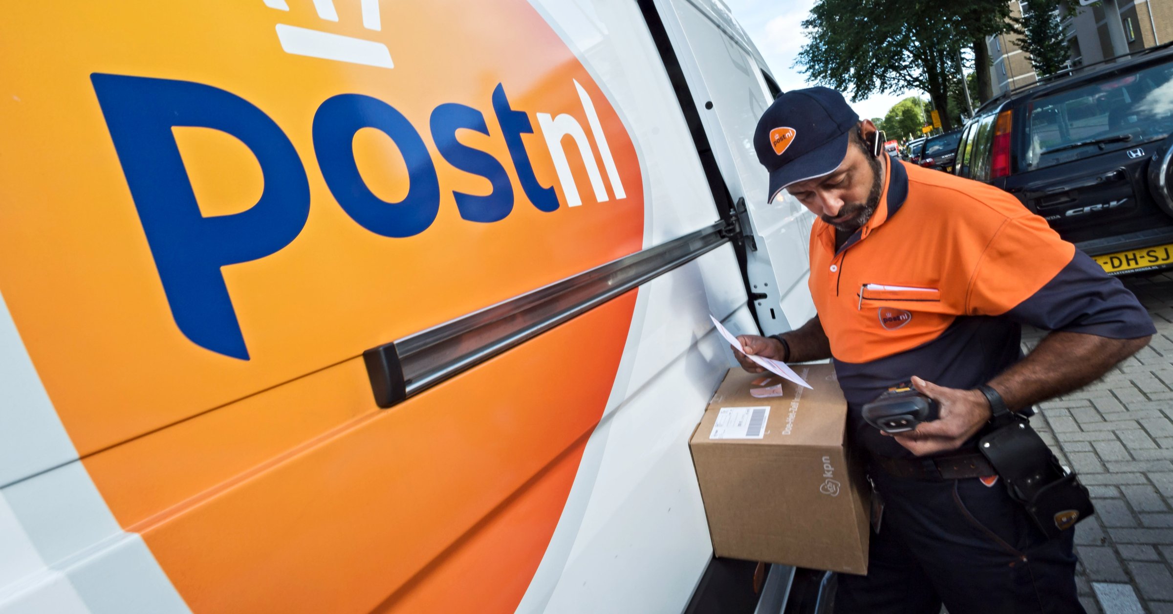 Een pakketbezorger van PostNL checkt de gegevens van een bestelling op zijn smartphone. Foto: Lex van Lieshout/ANP
