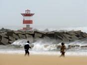 Wandelaars lopen in een zware storm over het strand bij de haven van Scheveningen.