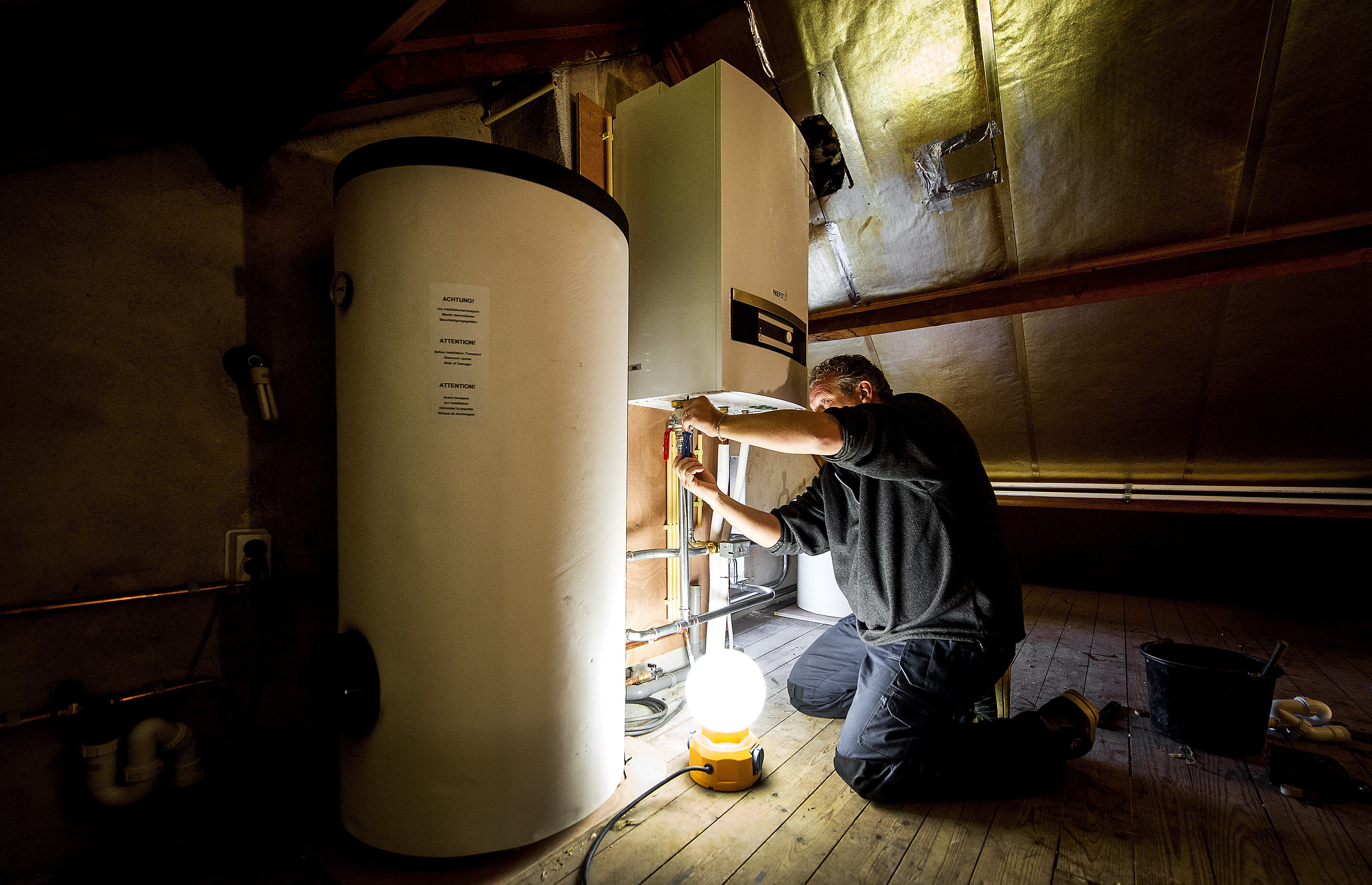 Een installateur is bezig met het installeren van een warmtepomp bij een verwarmingsketel.
