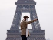 Een man met mondkapje neemt een selfie bij de Eiffeltoren in Parijs