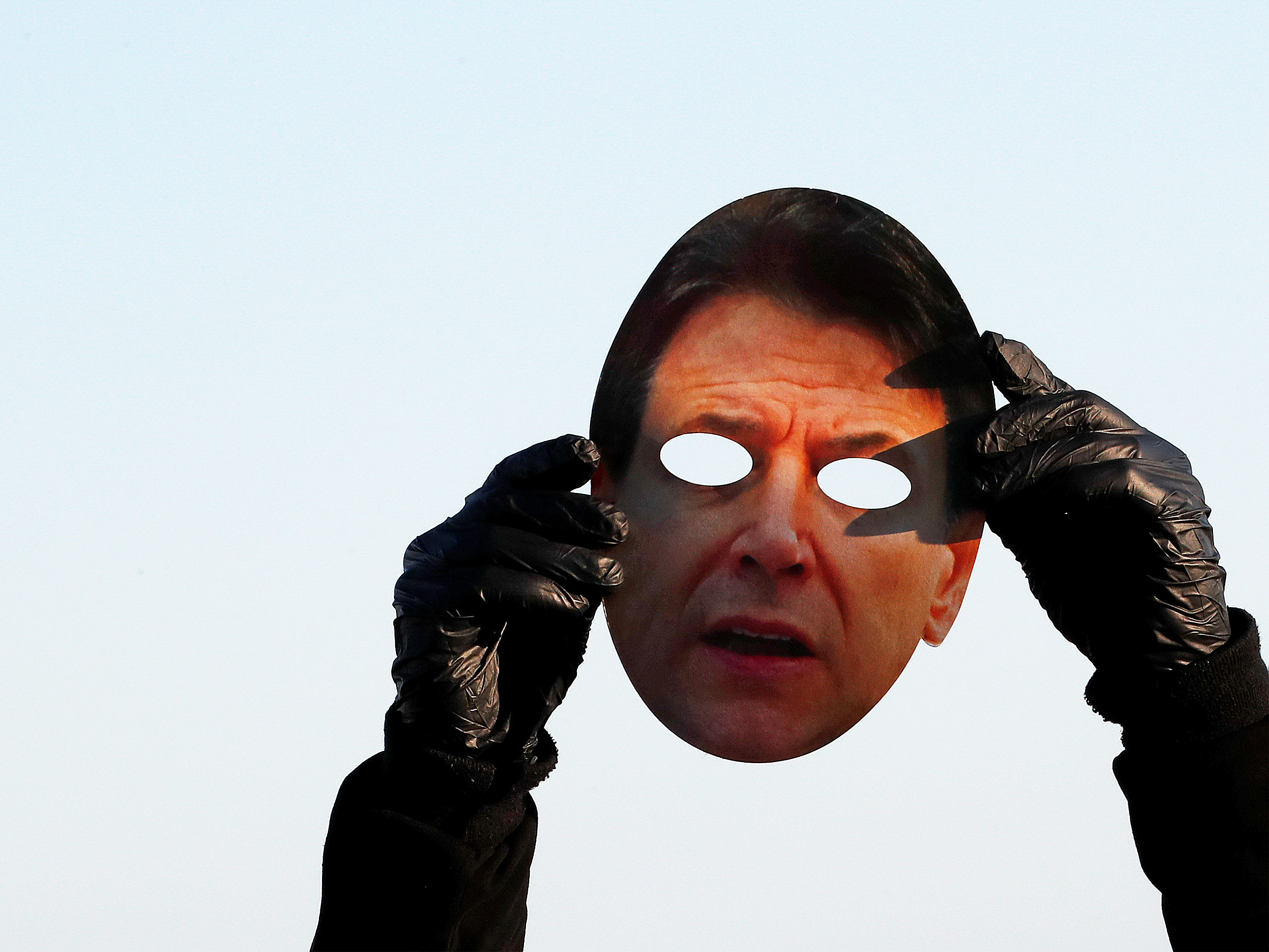 Een demonstrant houdt een masker van de Italiaanse premier Conte omhoog.