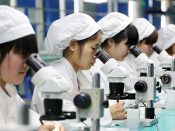 Vrouwen in een fabriek in Huaibei. Ze gebruiken een microscoop om kleine motoren voor in smartphones in elkaar te zetten.