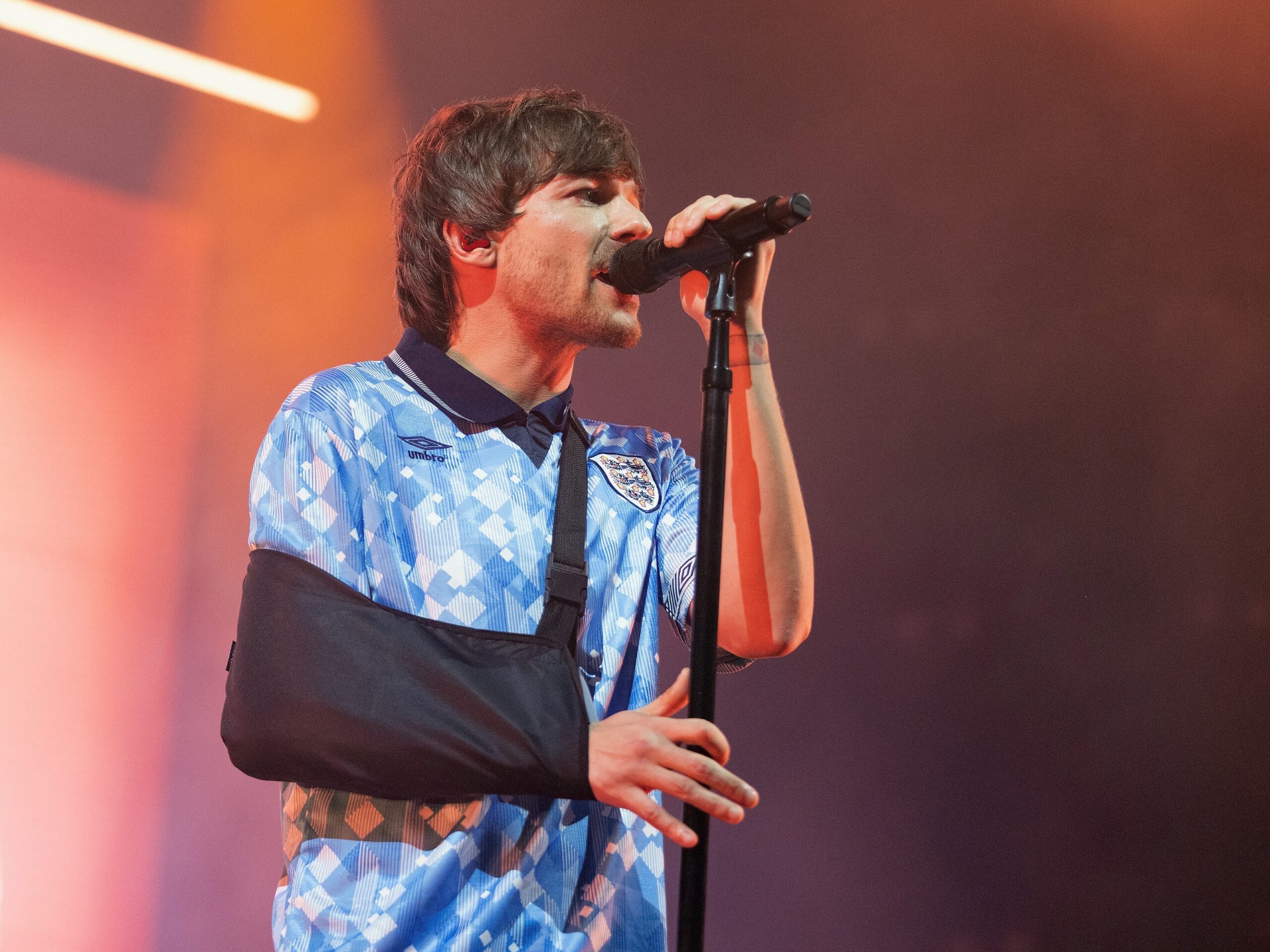 louis tomlinson with his arm in a cast performing on stage solo in 2022