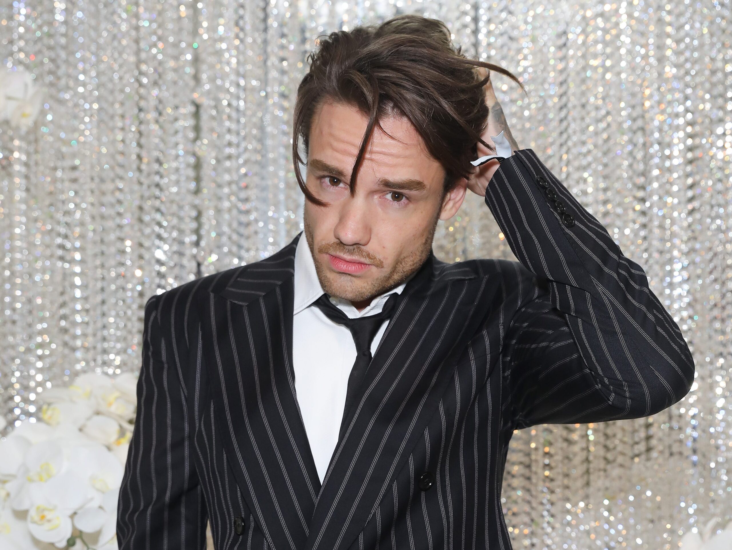 Liam Payne with long hair, strands over his face and hand on his head in a pinstripe suit