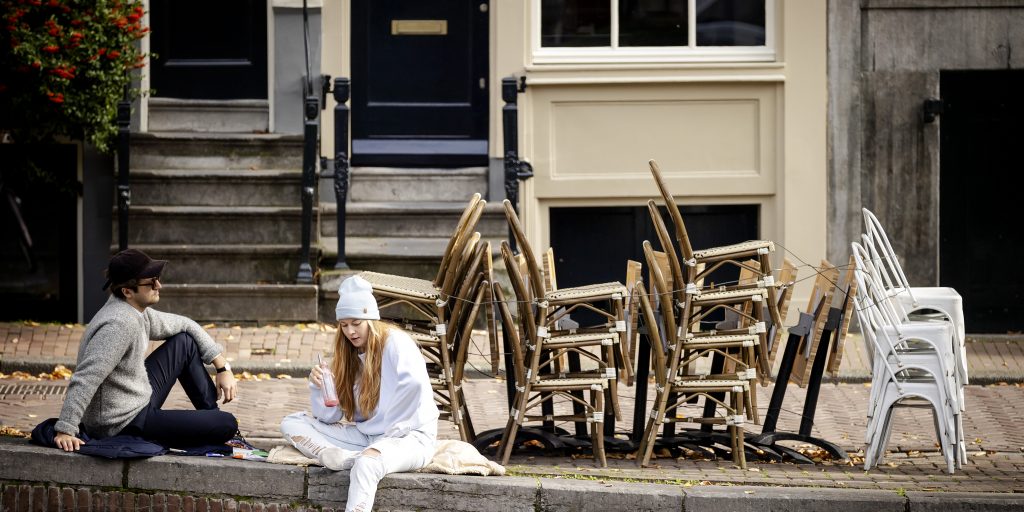 Mensen lunchen bij een stapel stoelen van een gesloten terras van een horecazaak in Amsterdam.