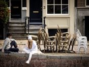 Mensen lunchen bij een stapel stoelen van een gesloten terras van een horecazaak in Amsterdam.