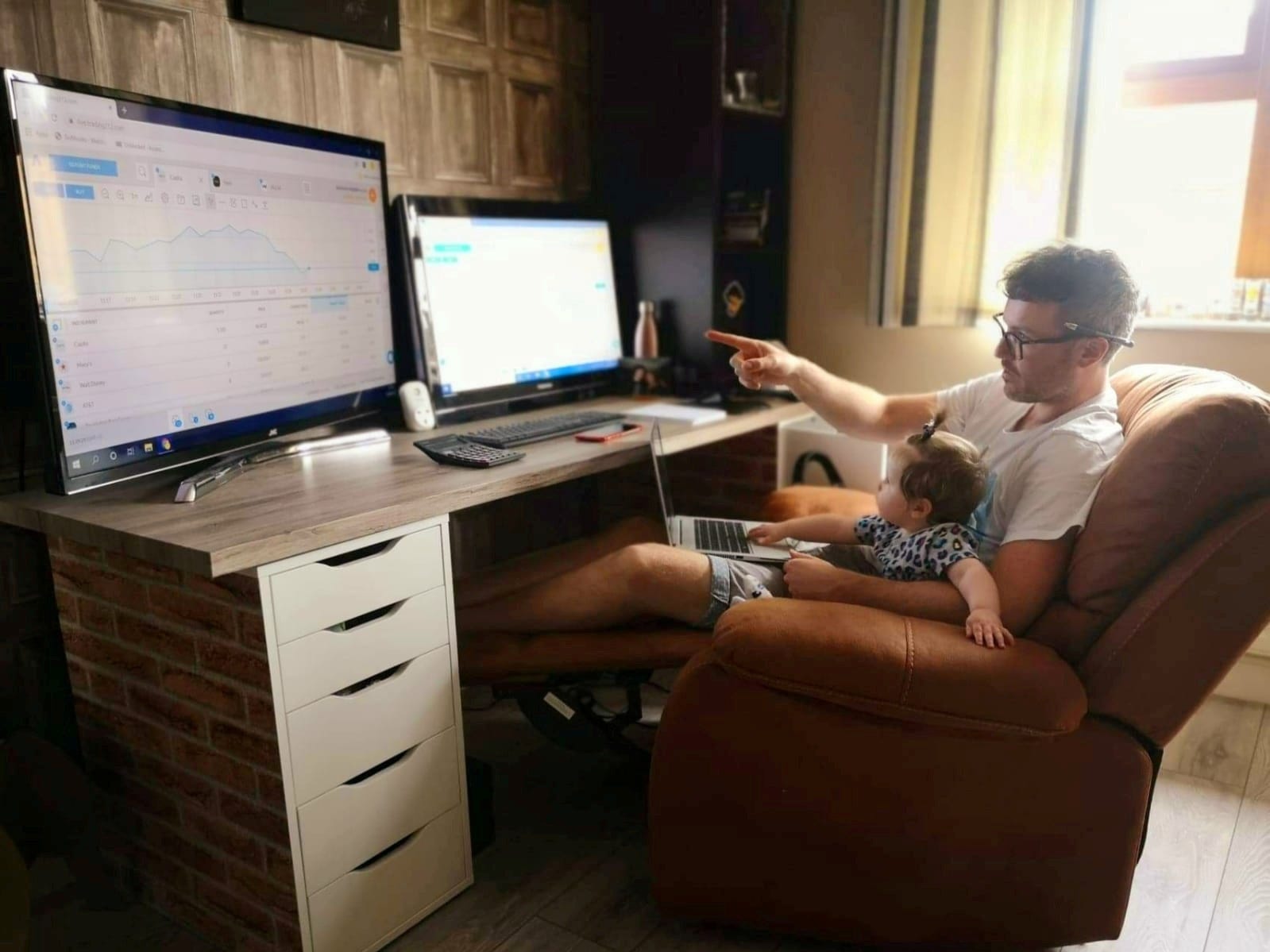 Daytrader Damian McVeigh sits in front of computers with his daughter Avril at home during the coronavirus disease (COVID-19) outbreak, in Belfast, Northern Ireland June 16, 2020.
