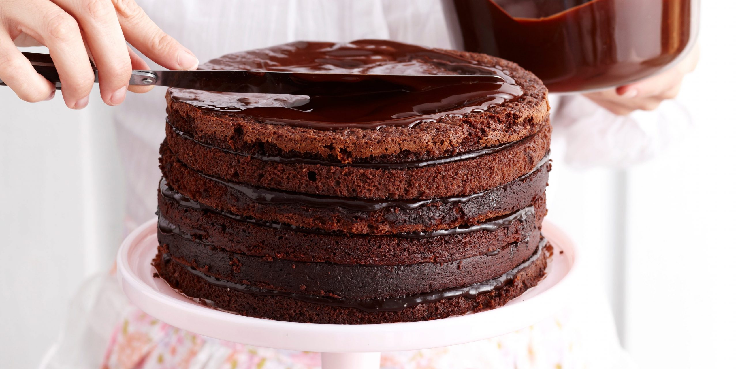 woman icing layered chocolate cake