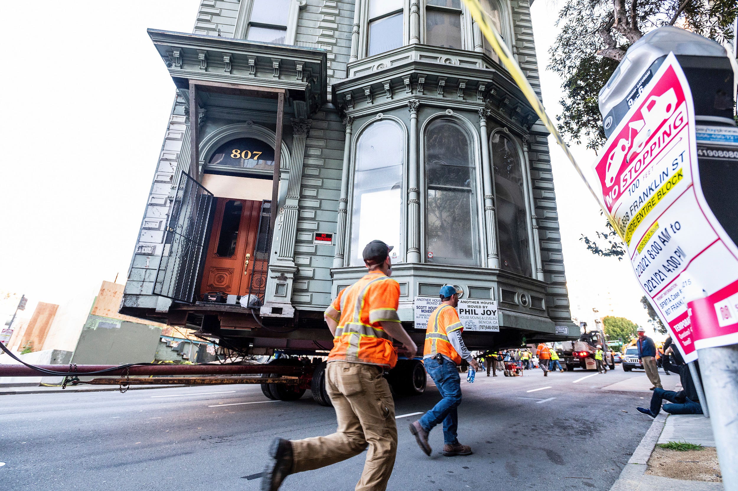 Workers pass a Victorian home as a truck pulls it through San Francisco on Sunday, Feb. 21, 2021.