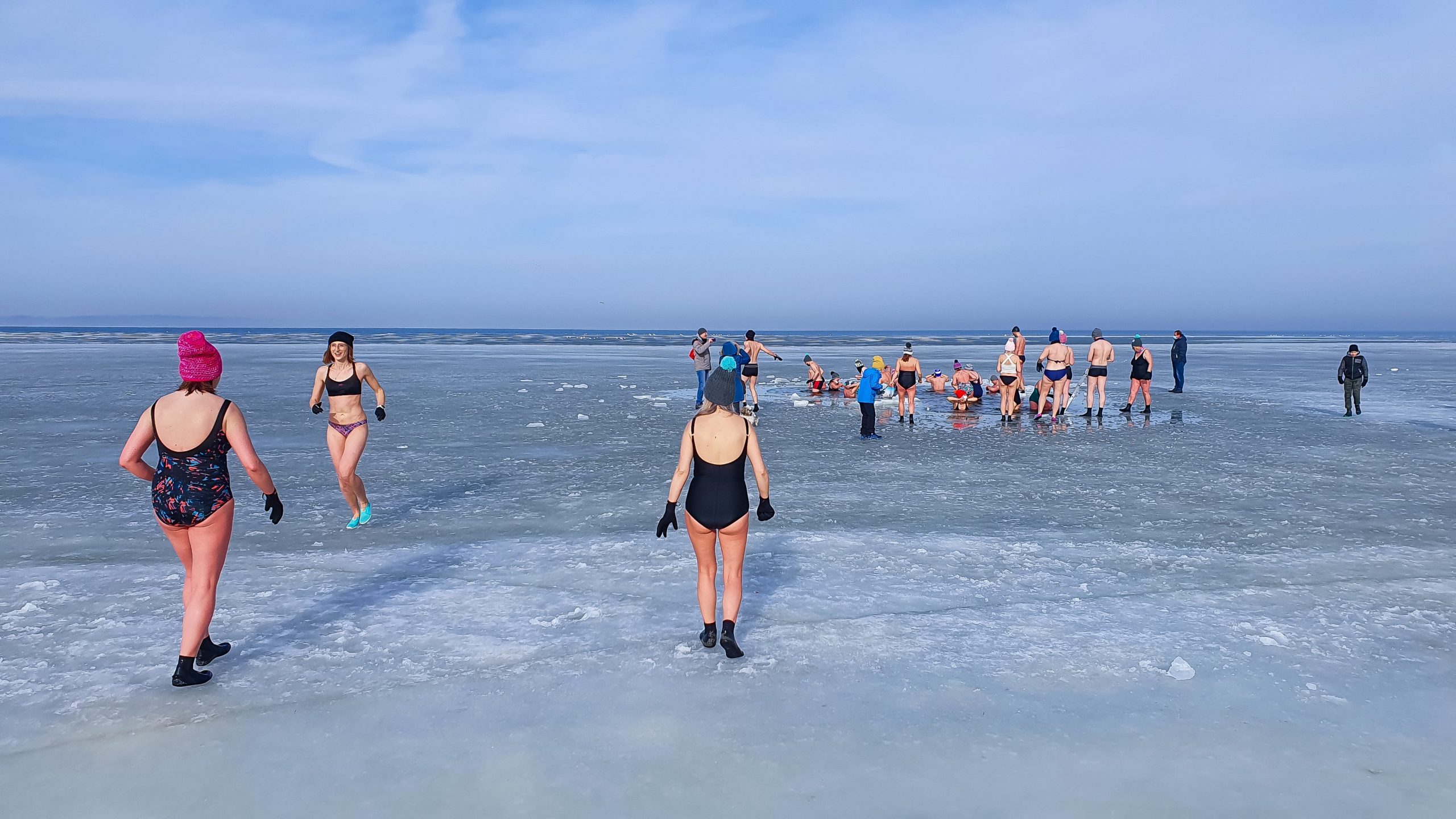 Winter swimming. People winter bathing in the sea. A large group of people is walking on frozen water.