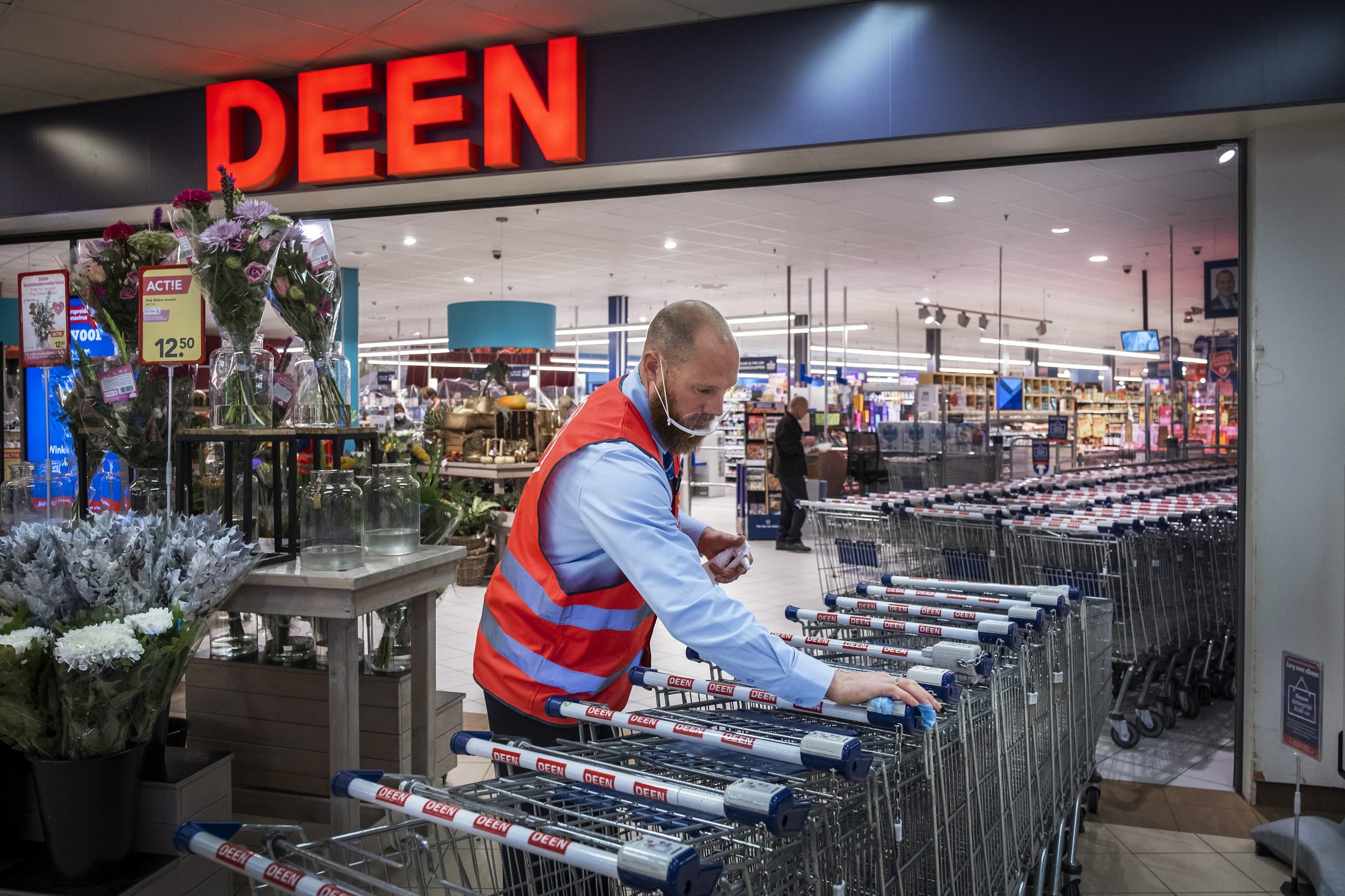 Een medewerker van supermarkt Deen maakt de winkelwagentjes schoon.