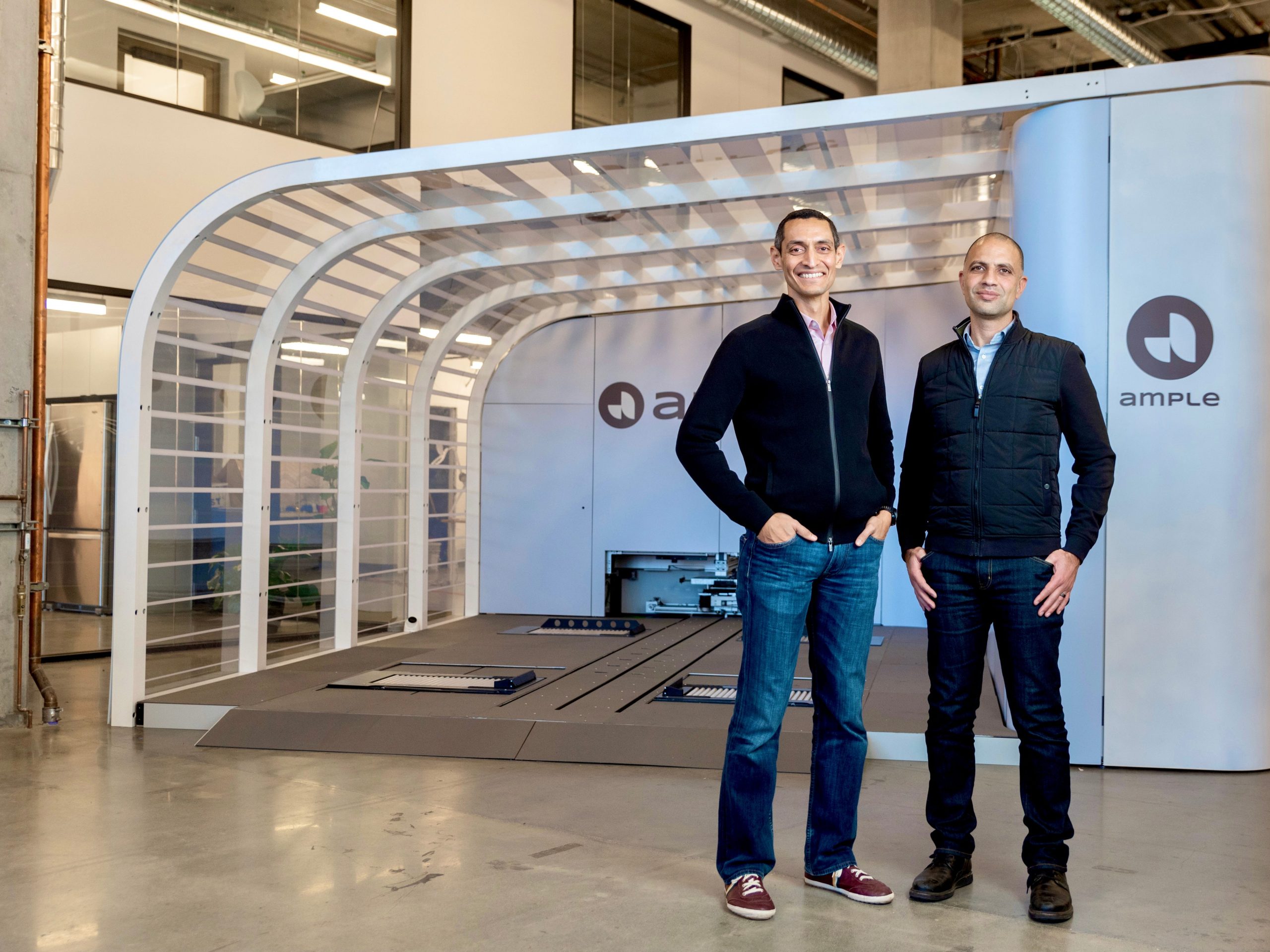 Ample founders Khaled Hassounah and John de Souza stand in front of a battery swapping station.