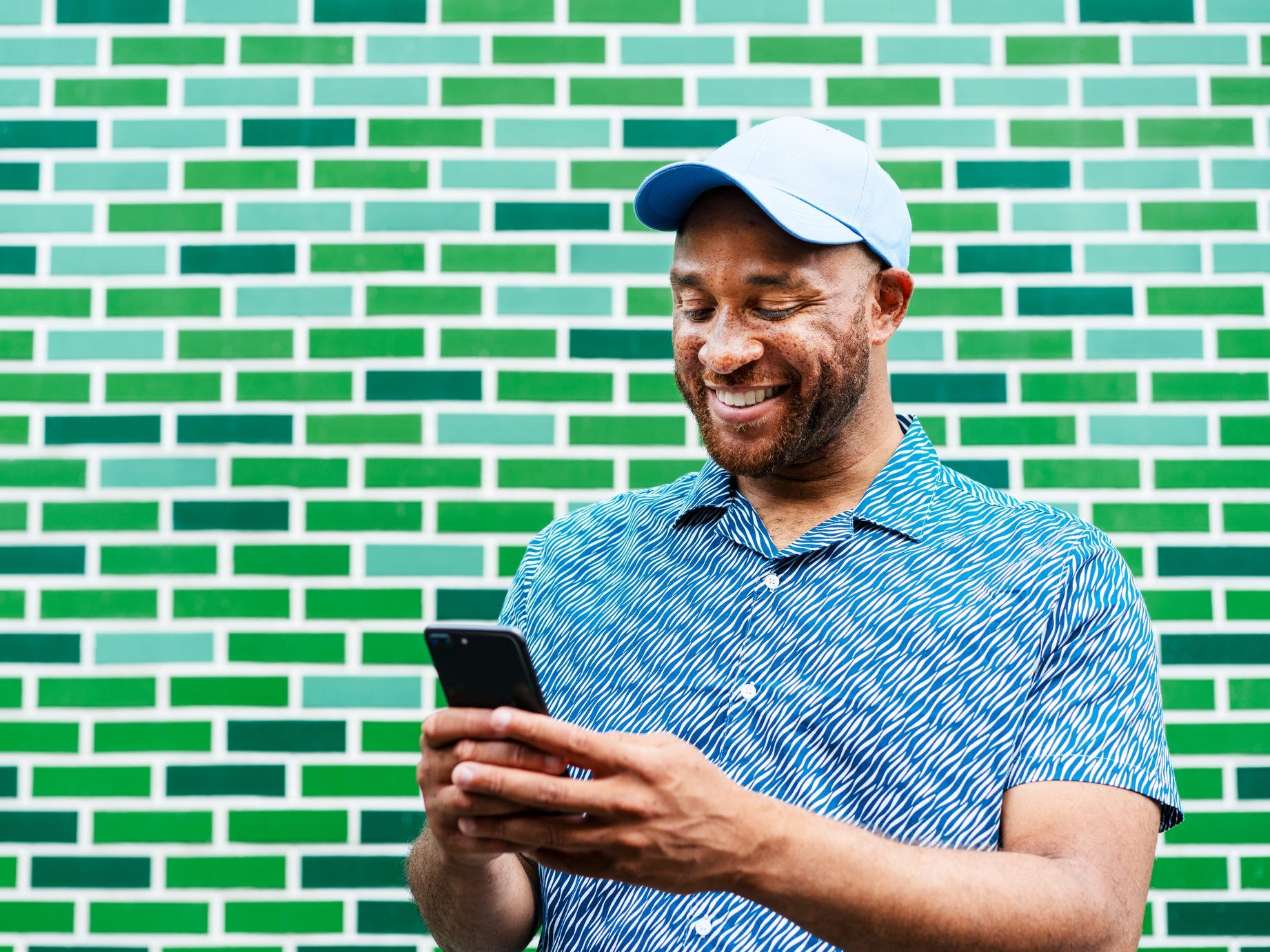 Man with cell phone in front of green bricks