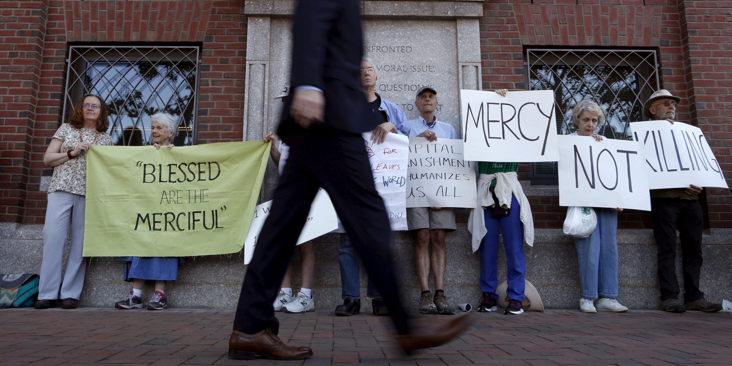 FILE PHOTO: A pedestrian walks past death penalty protesters before the formal sentencing of convicted Boston Marathon bomber Dzhokhar Tsarnaev at the federal courthouse in Boston, Massachusetts June 24, 2015. REUTERS/Dominick Reuter/File Photo