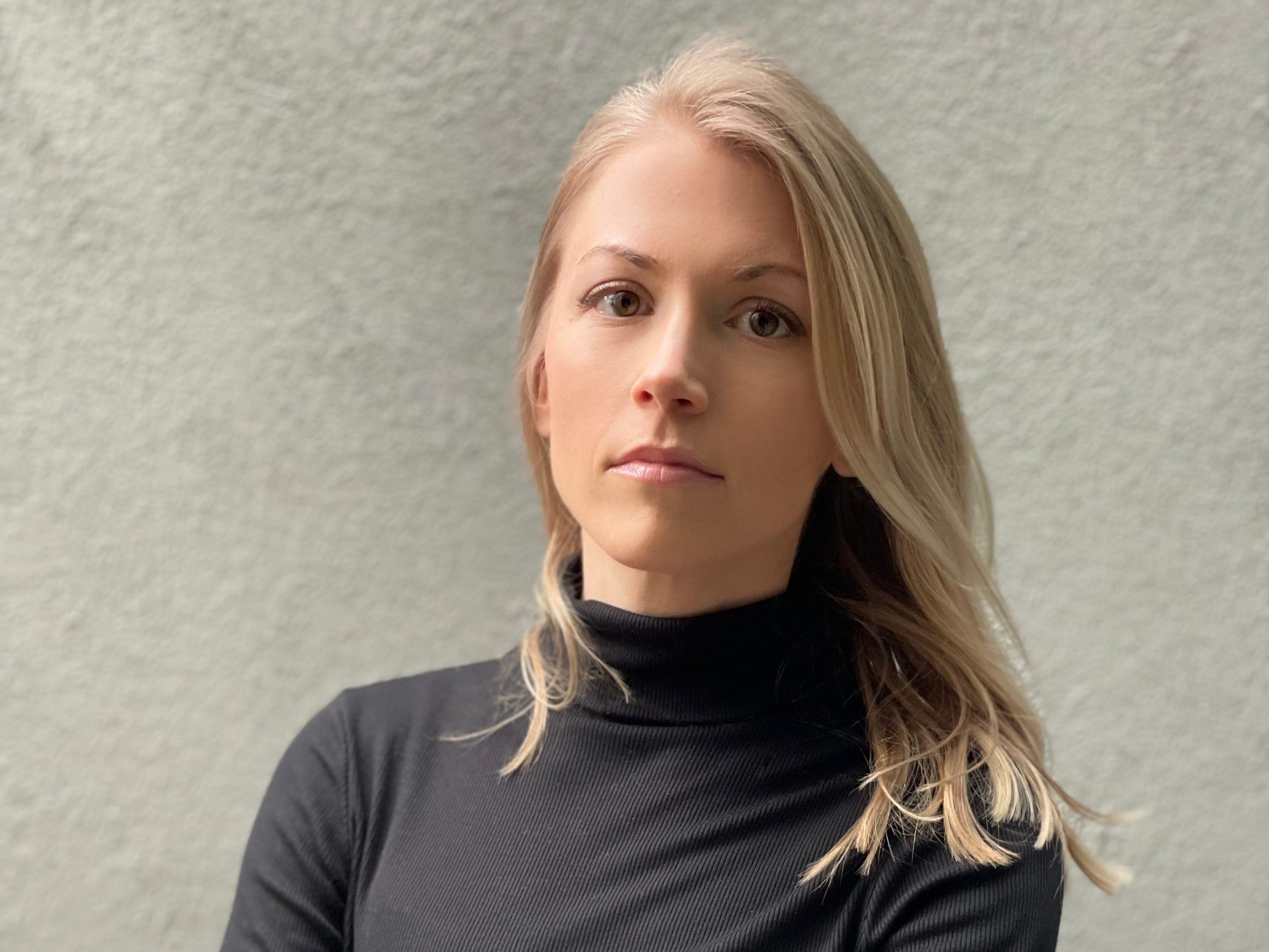 Ashley Frederes stands with arms crossed in front of a blank wall