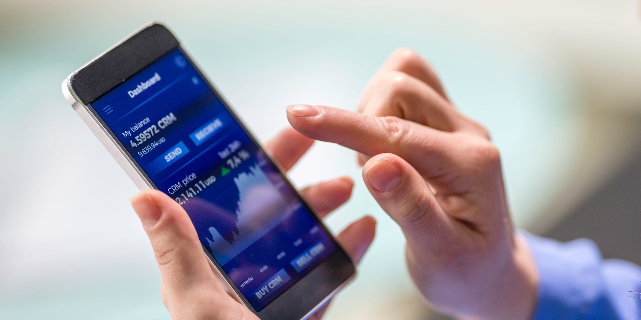 Close-up photo of a woman buying cryptocurrency through a smart phone app that is also showing the growth graph.