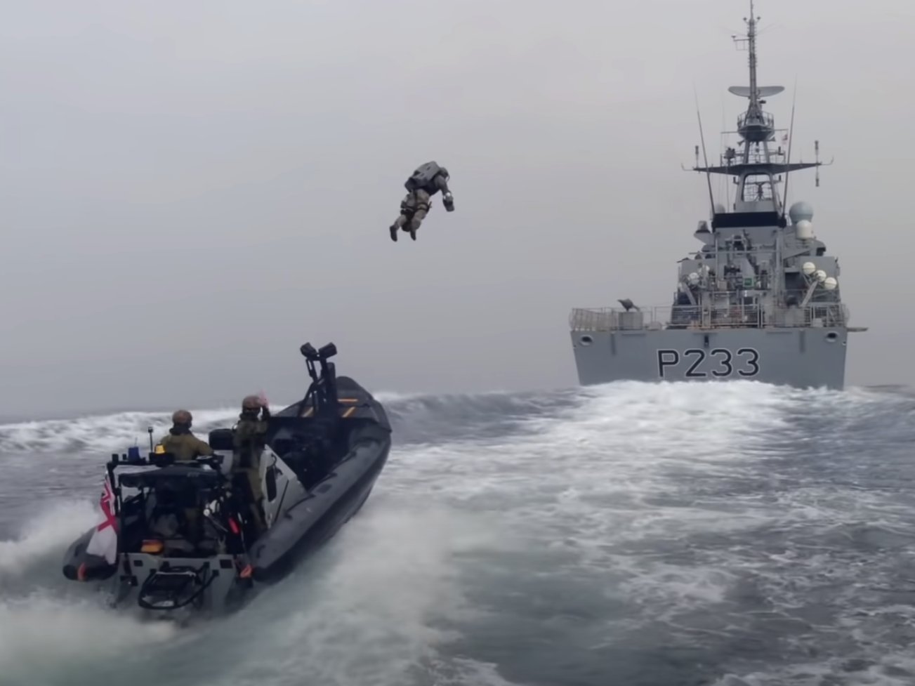 A Royal Marine in a jetpack launches from a fast boat to board a Royal Navy ship.