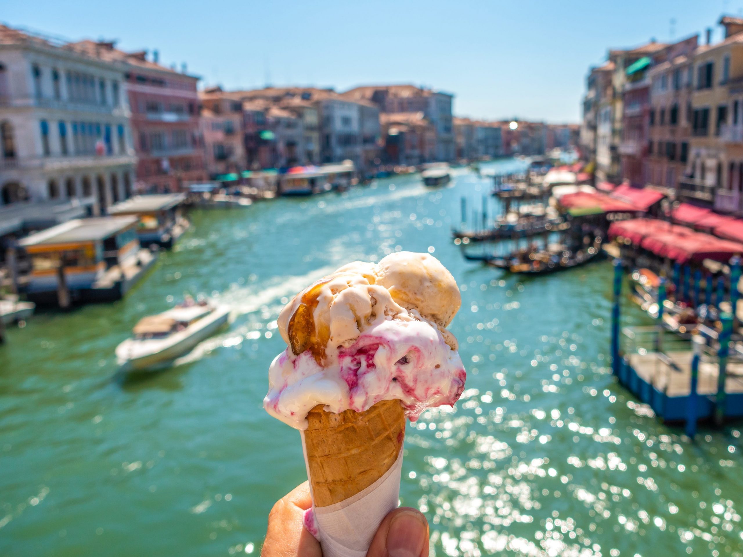 A person holds a cone of gelato over blue water in Italy