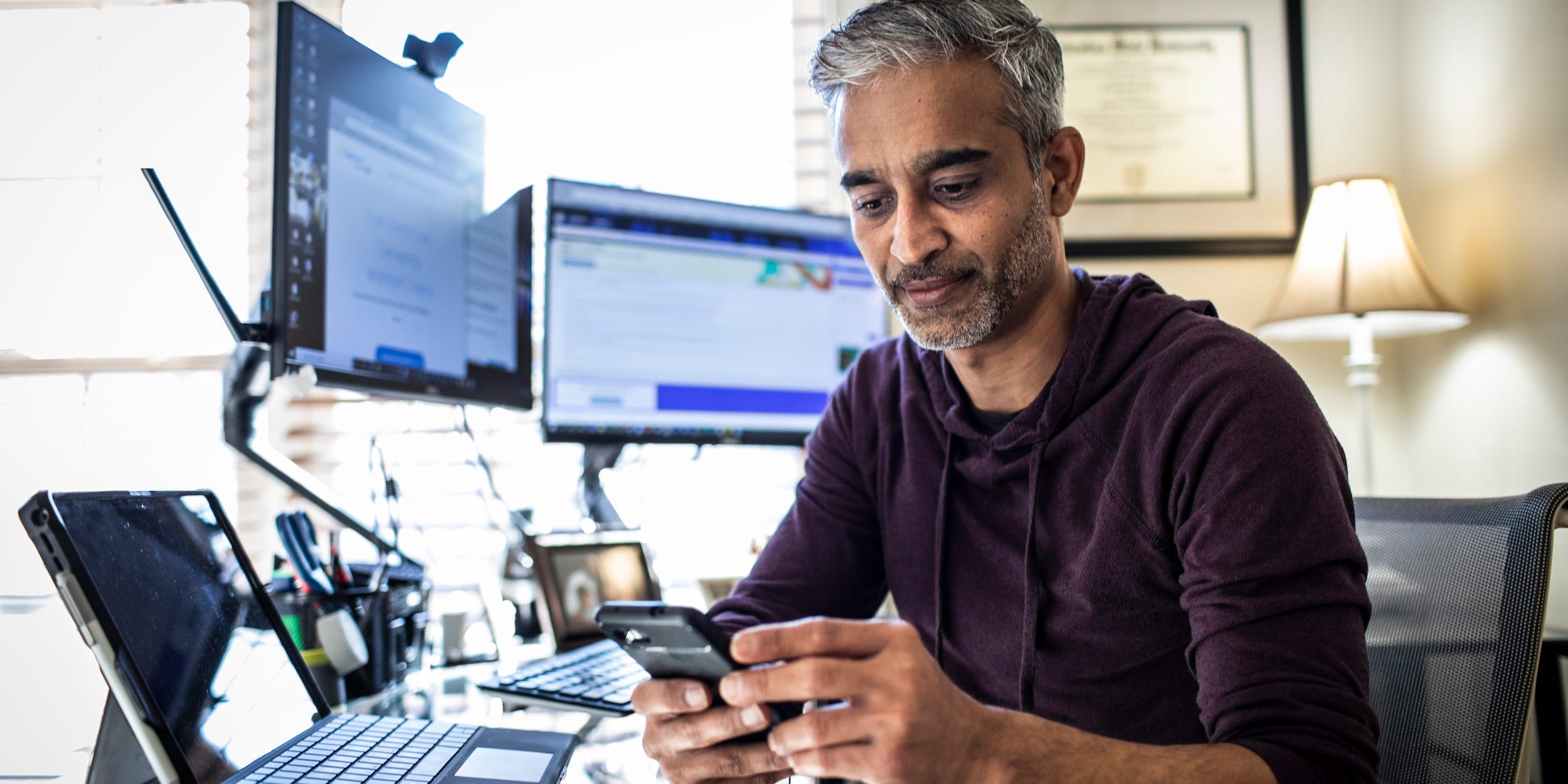 man using phone and several computer screen desktop laptop