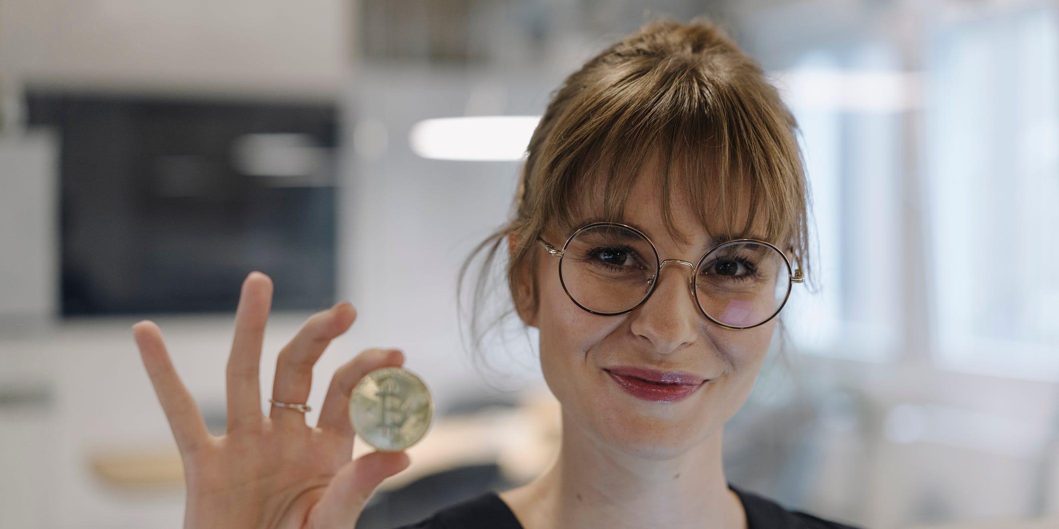 A woman standing in an office is holding a bitcoin in her hand.
