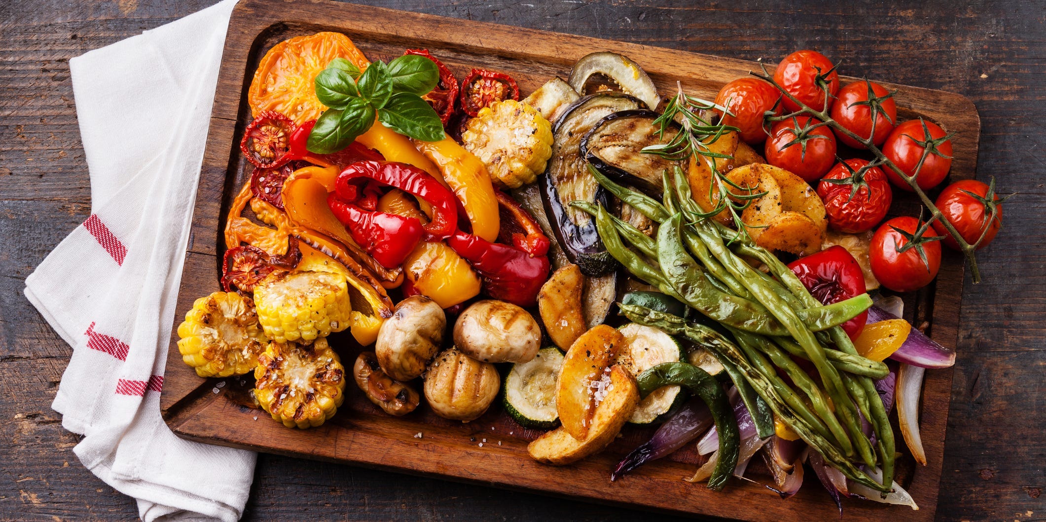 Platter of grilled vegetables including corn, tomatoes, mushrooms, and peppers