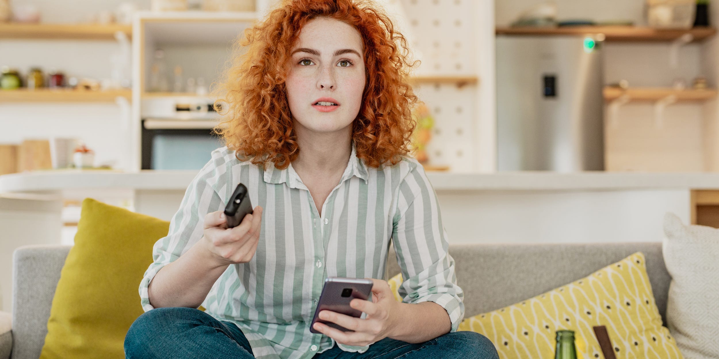 woman on couch holding smartphone and tv remote