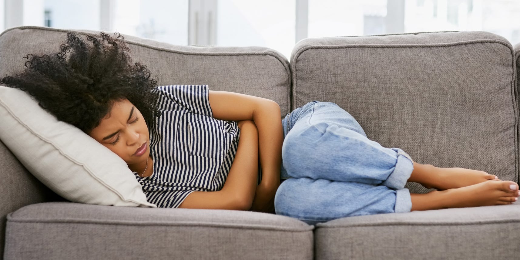 woman with cramps clutching stomach in pain on couch