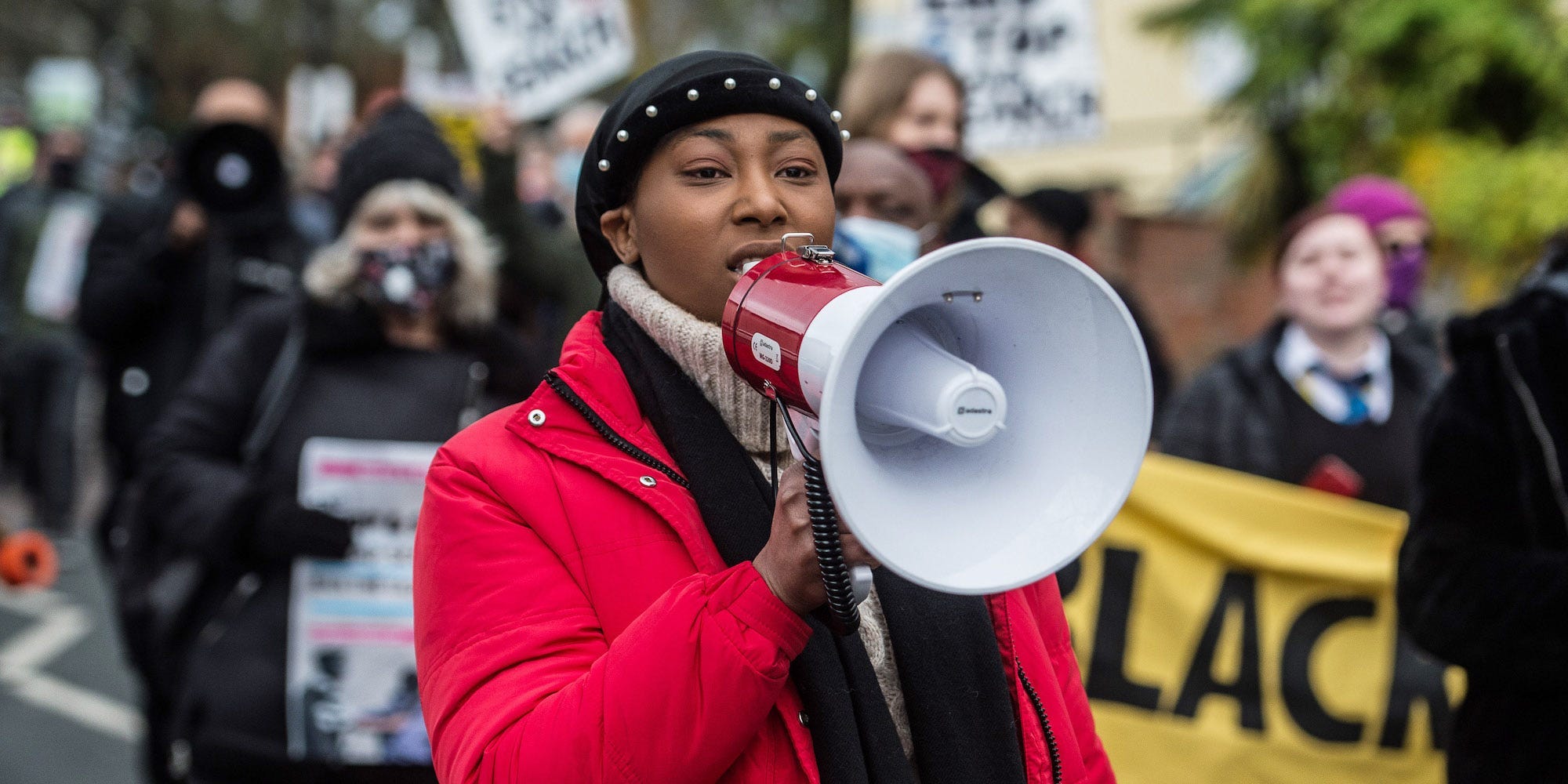 Sasha Johnson holding a megaphone at a 2020 Black Lives Matter Protest, with protesters in the background.