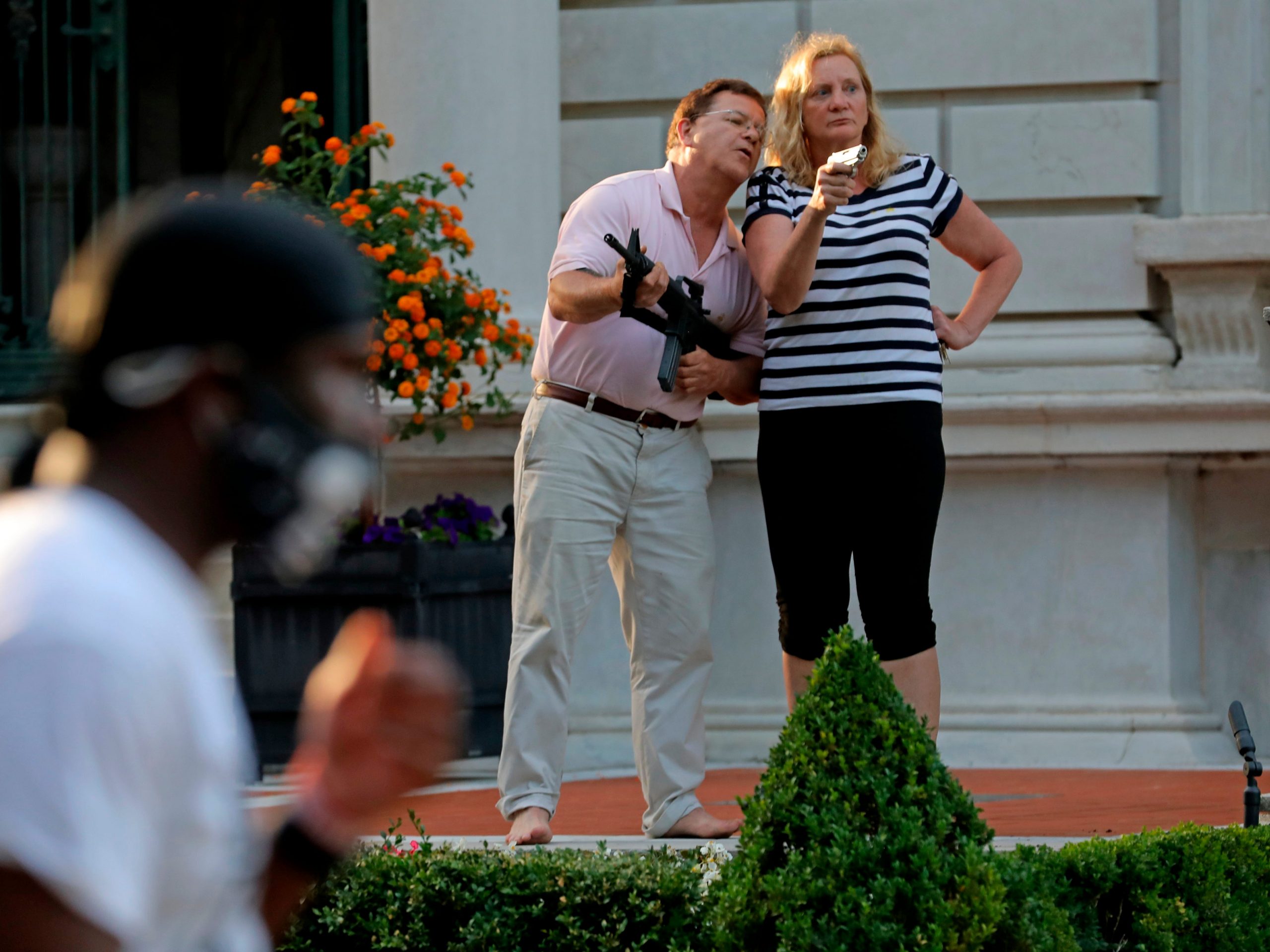 FILE - In this June 28, 2020 file photo, armed homeowners Mark and Patricia McCloskey, standing in front their house along Portland Place confront protesters marching to St. Louis Mayor Lyda Krewson's house in the Central West End of St. Louis. Authorities executed a search warrant Friday evening, July 10, 2020, at the St. Louis mansion owned by the McCloskey's, a white couple whose armed defense of their home during a racial injustice protest last month made national headlines. said. Joel Schwartz, who is now representing the couple, confirmed on Saturday that a search warrant was served, and that the gun Mark McCloskey was seen holding during last month's protest was seized. (Laurie Skrivan/St. Louis Post-Dispatch via AP)