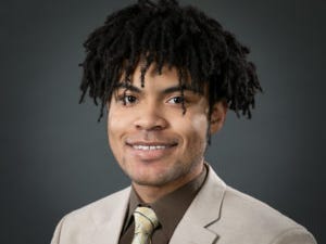 Elijah Armstrong: A young man of color in a suit smiling at the camera.