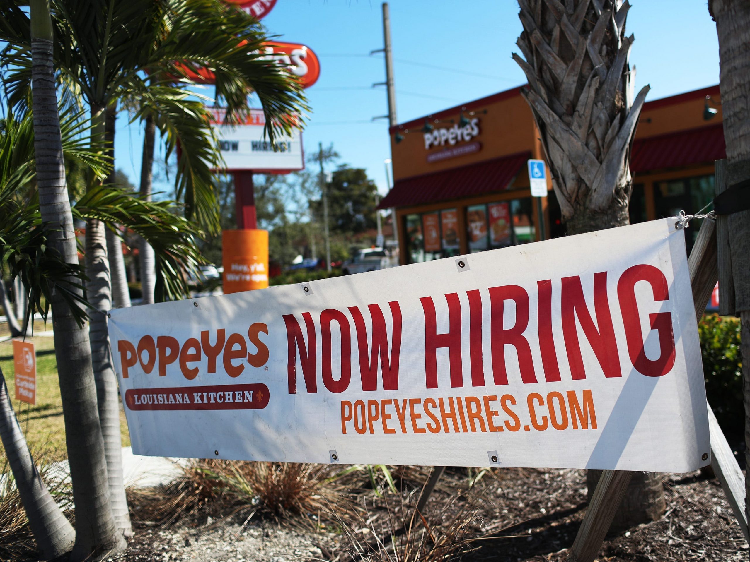 A "now hiring" sign hangs in front of a Popeyes location