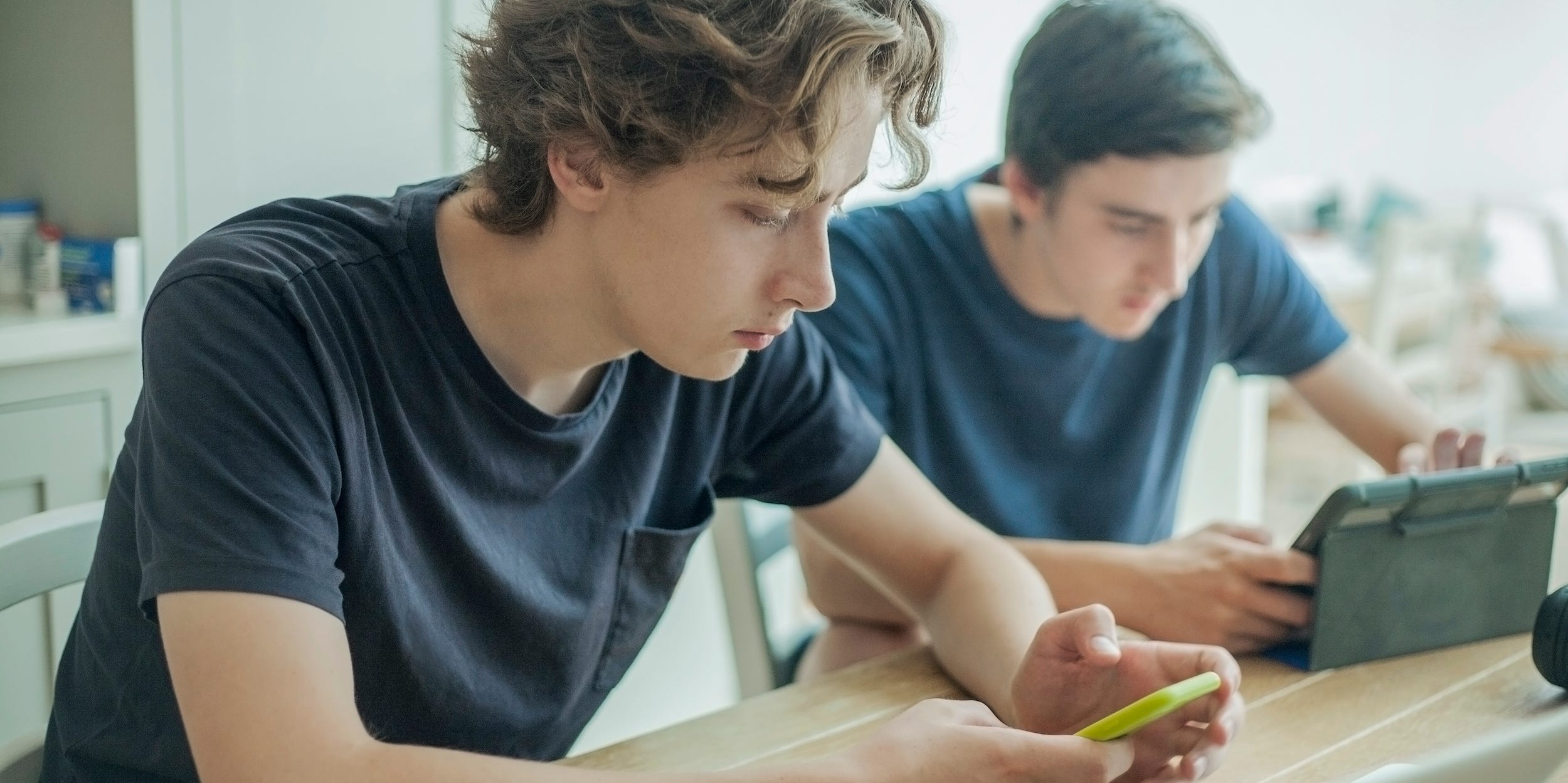 teens using phone and laptop at home working together