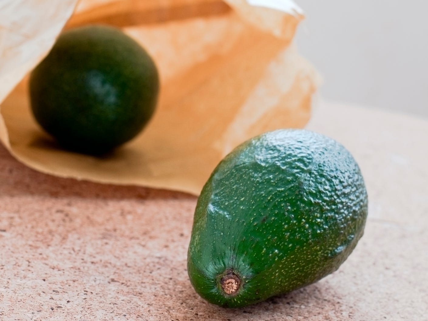 An avocado in a paper bag with another avocado in the foreground