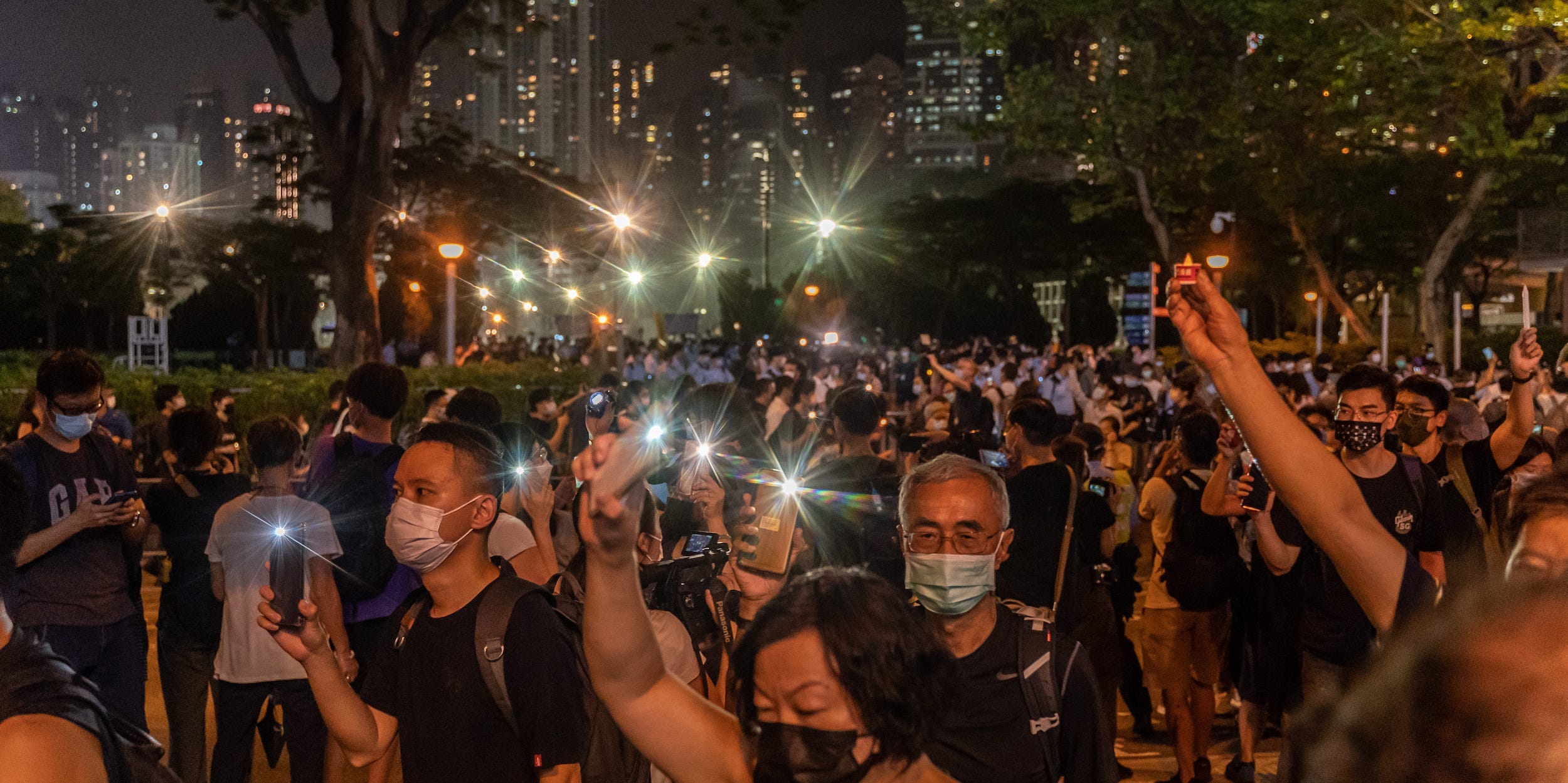 People hold up their phones with the light as they walk near the Victoria Park after police closed the venue where Hong Kong people traditionally gather annually to mourn the victims of China's Tiananmen Square crackdown in 1989, in the Causeway Bay district on June 4, 2021 in Hong Kong, China.