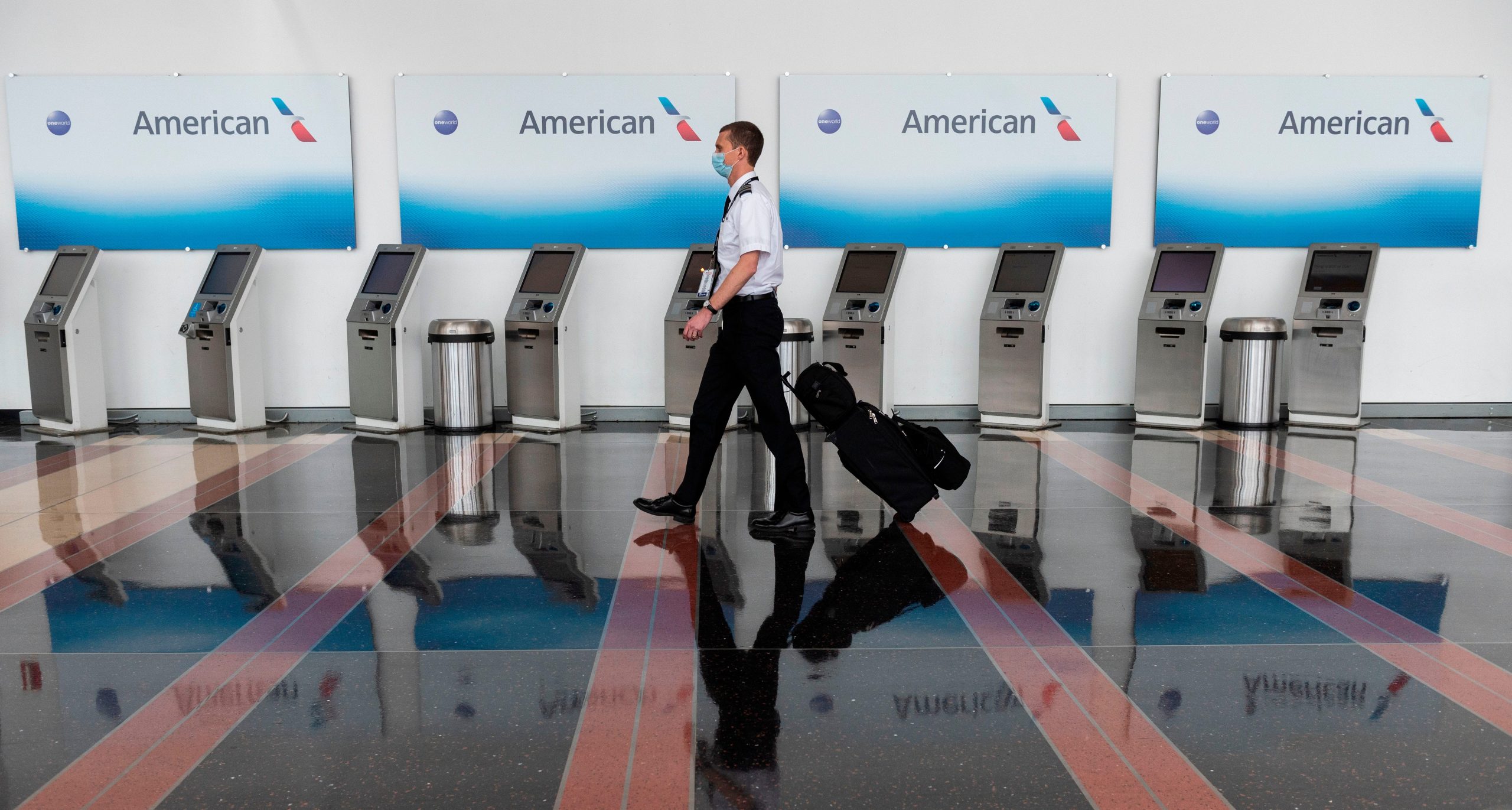 An airline employee walks past empty American Airlines check-in terminals at Ronald Reagan Washington National Airport in Arlington, Virginia, on May 12, 2020. - The airline industry has been hit hard by the COVID-19 pandemic, with the number of people flying having decreased by more than 90 percent since the beginning of March.