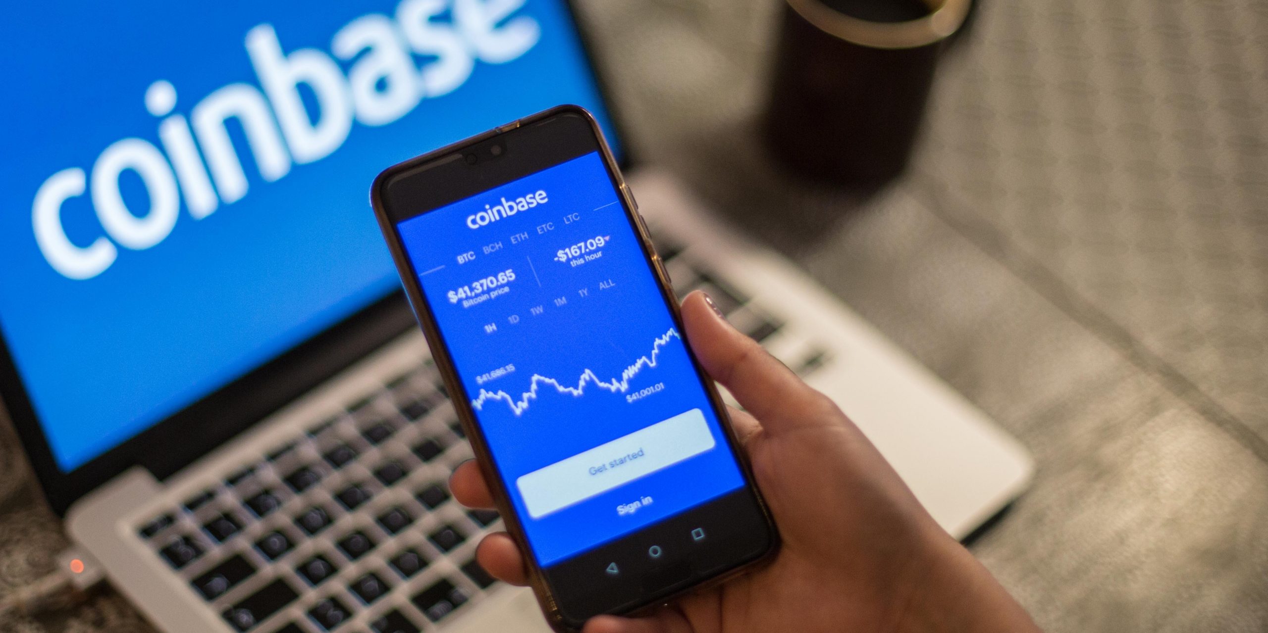 Coinbase app on phone in front of laptop with Coinbase logo