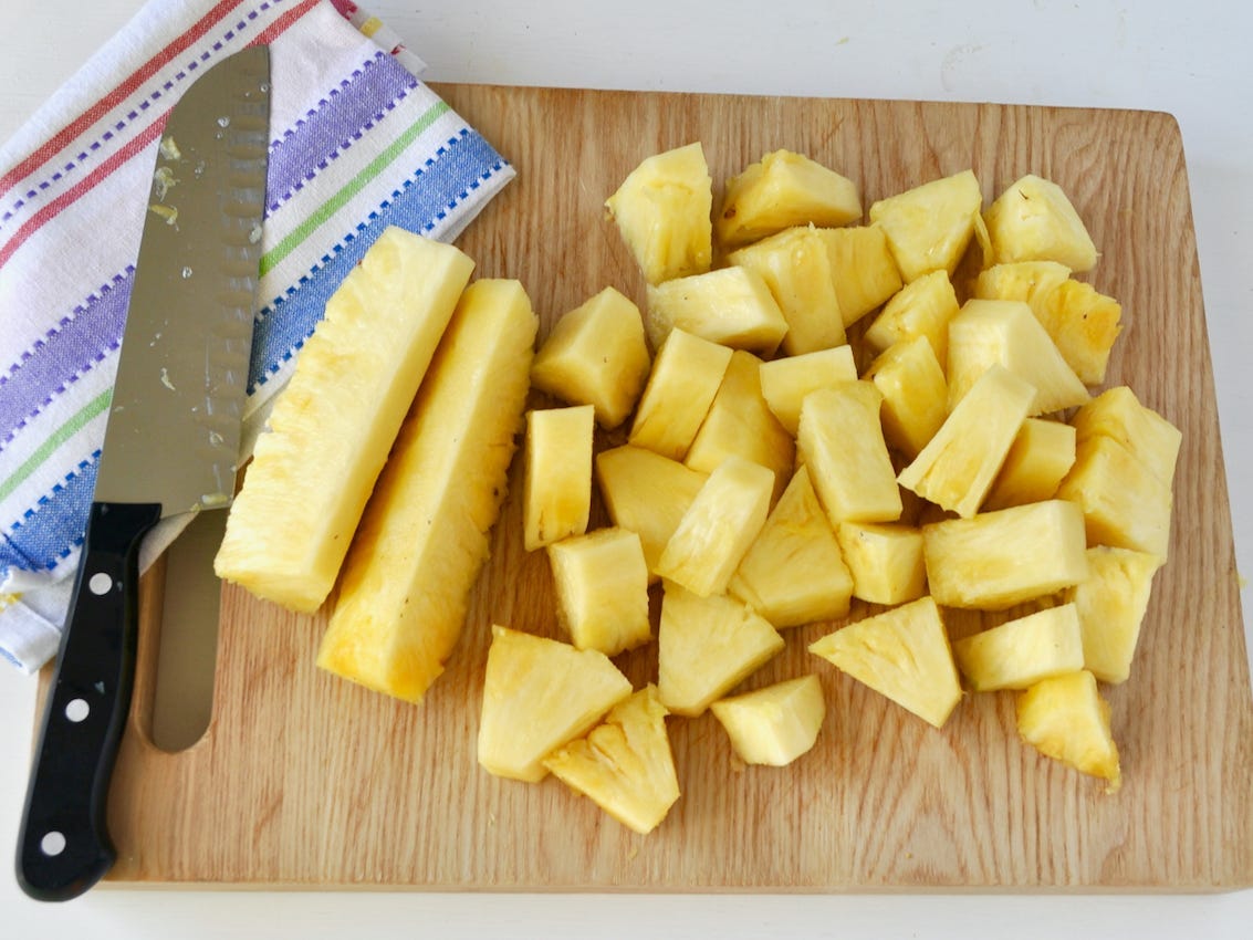 Pineapple cut into spears and chunks on a cutting board with a knife and towel