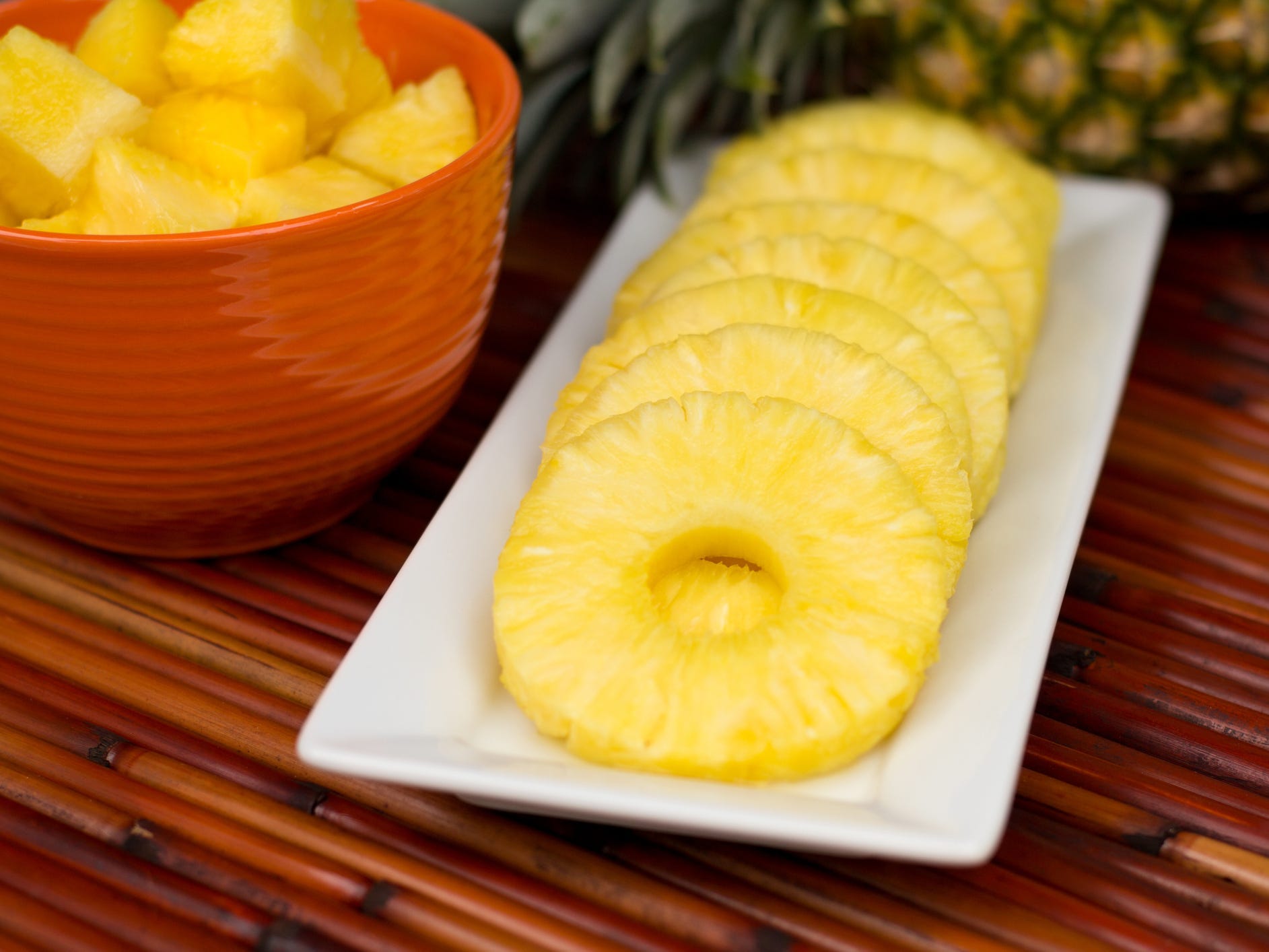 Pineapple rings lined up on a plate with a bowl of pineapple chunks to its left