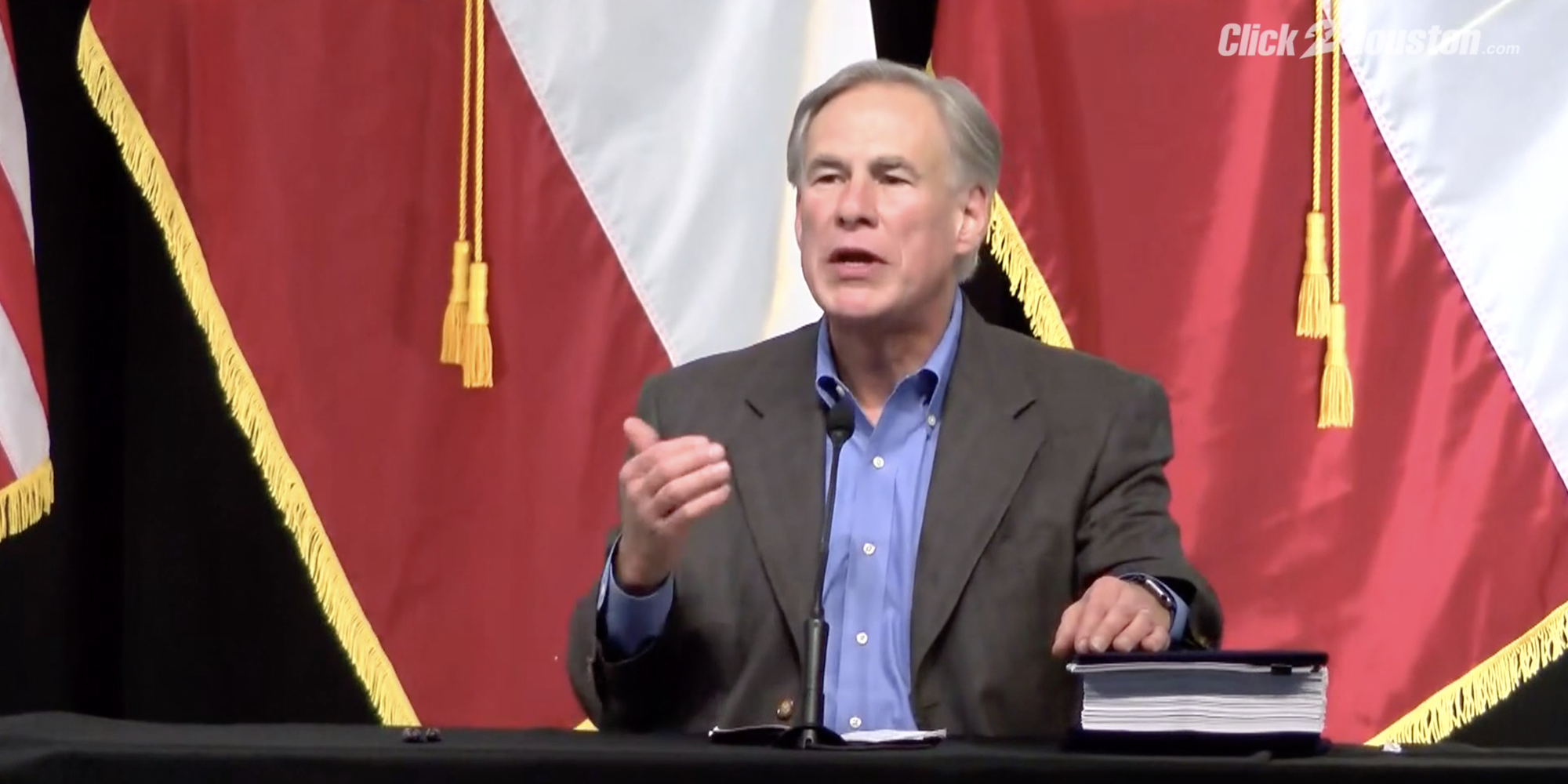 GOP Gov. Greg Abbott speaking at a border security press conference, with flags behind him.