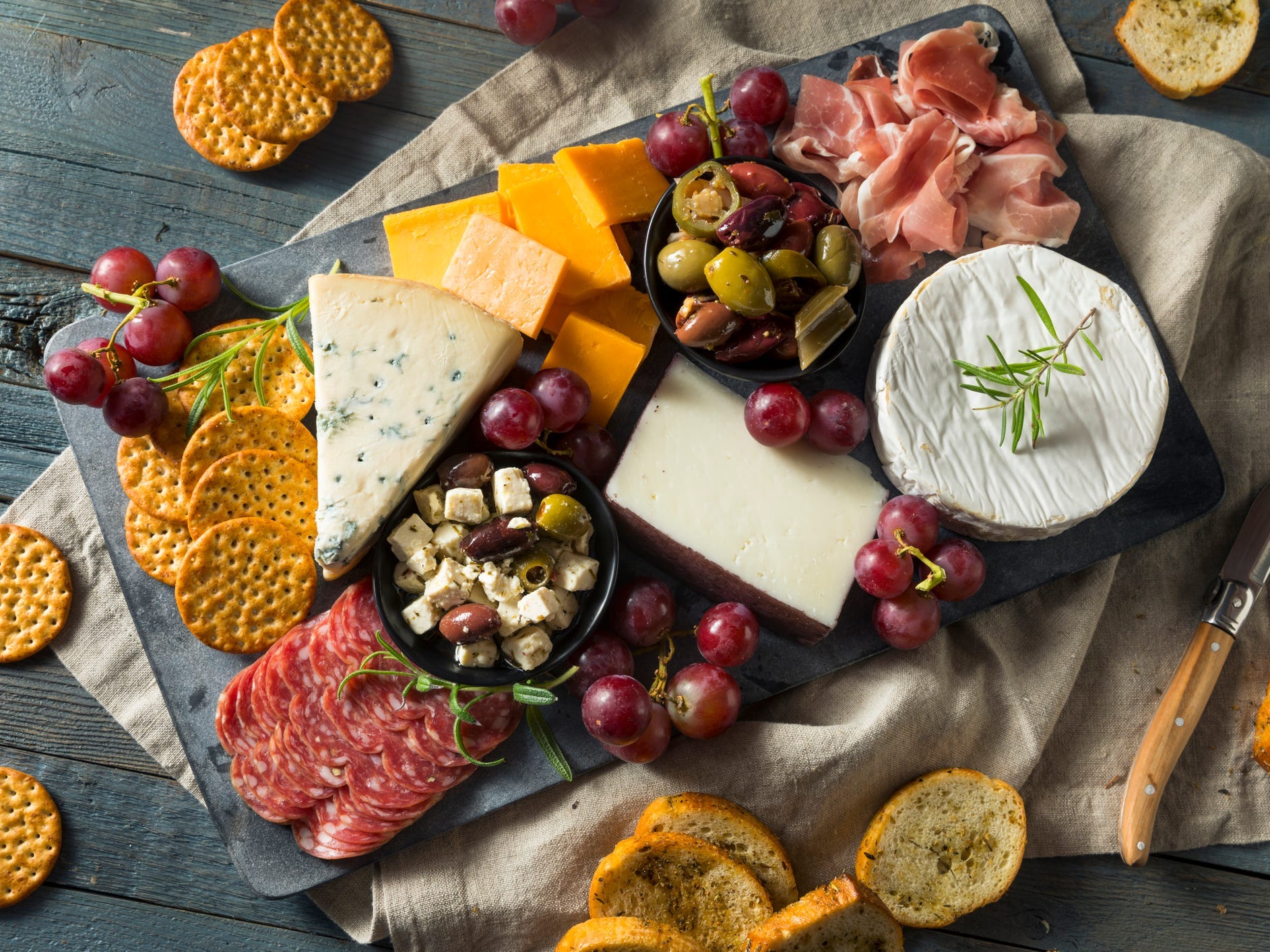 A charcuterie and cheese board with crackers, grapes, and olives