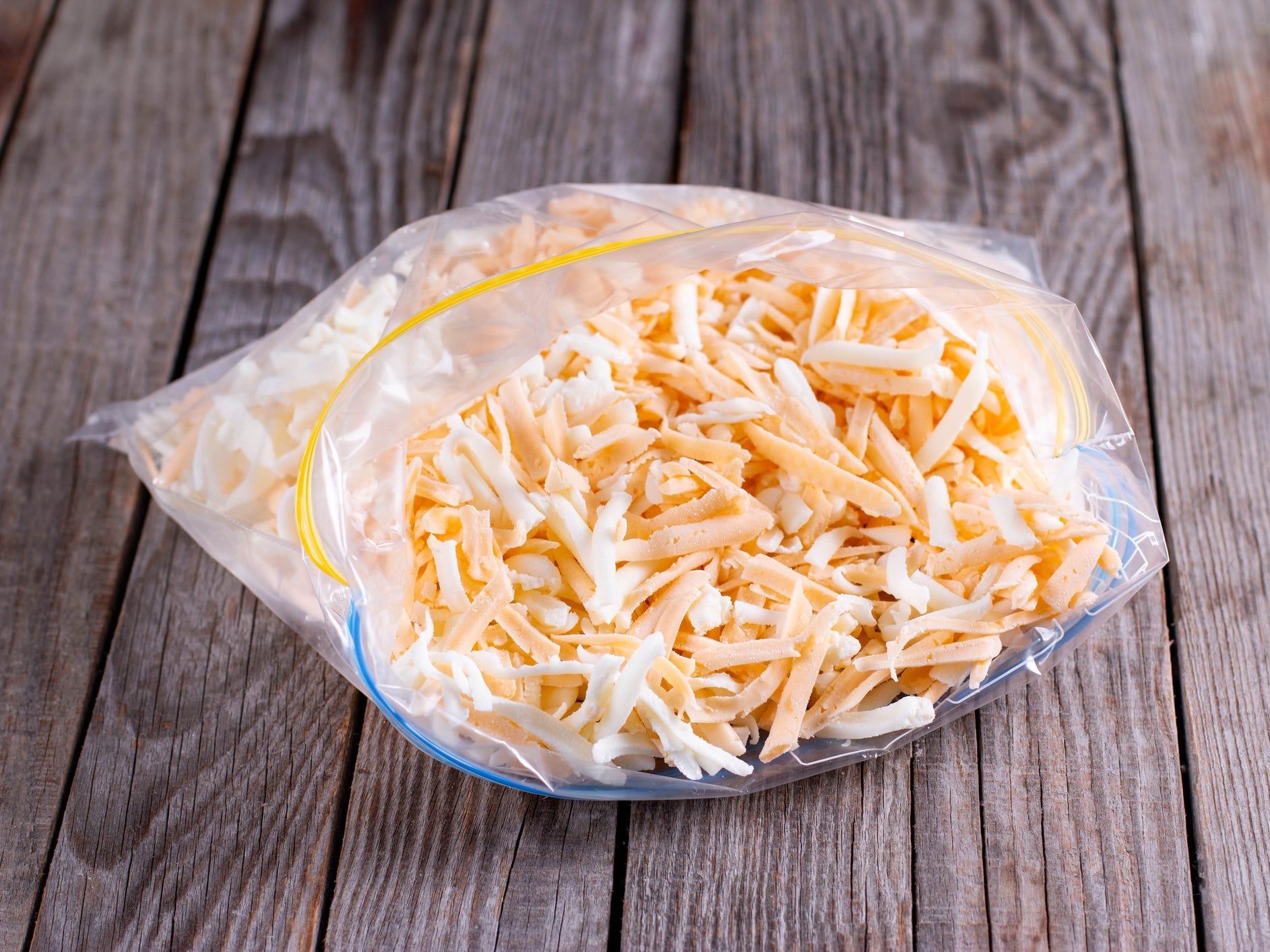 Frozen shredded cheese in an open baggie on a wooden table