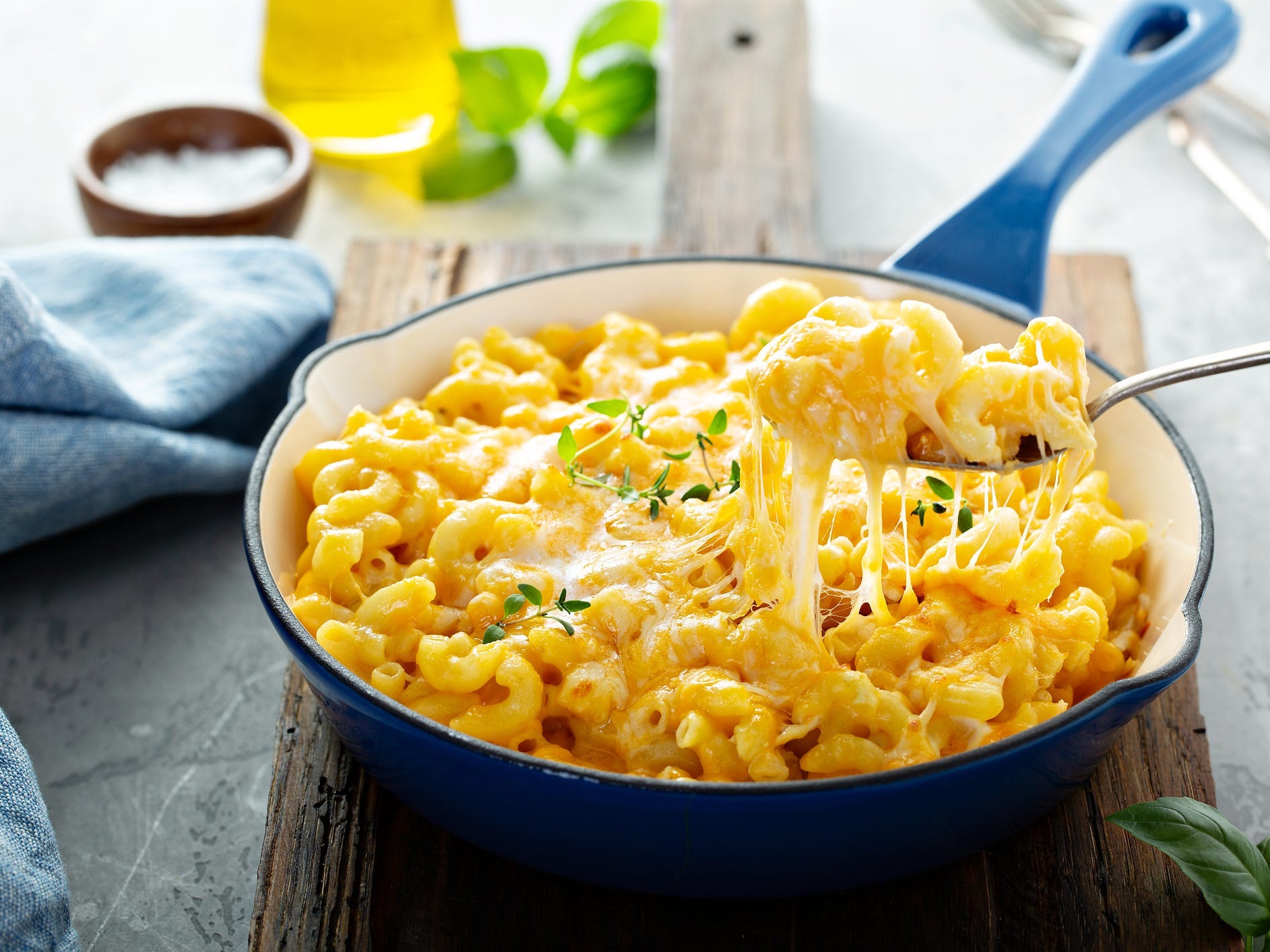 A fork holding a large bite of macaroni and cheese out of a blue skillet full of it