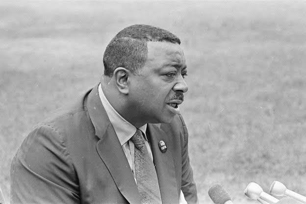 a man in a suit speaks into microphones in a black and white photo