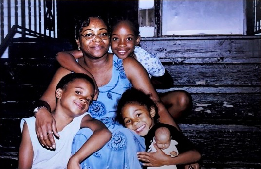 a mom and her three young kids embrace each other while posing for a photo on steps outside