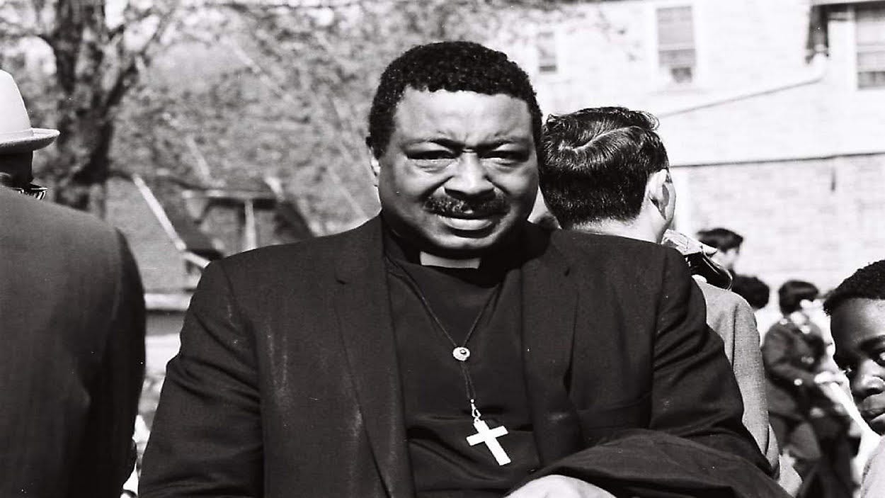 a reverend is seen in a black and white photo wearing a clerical collar with a cross around his neck