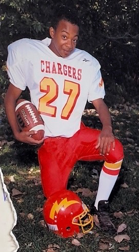 a young boy poses in his football uniform holding a football with a helmet at his feet